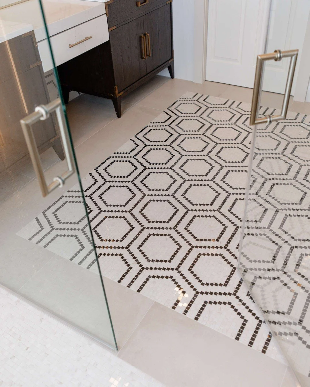 Just as a rug anchors a space, this bold hexagon mosaic tile grounds the design of this large primary bathroom. The black-and-white pattern adds visual interest and defines the area &mdash; creating the look of an inlaid &ldquo;tile rug&rdquo; that e