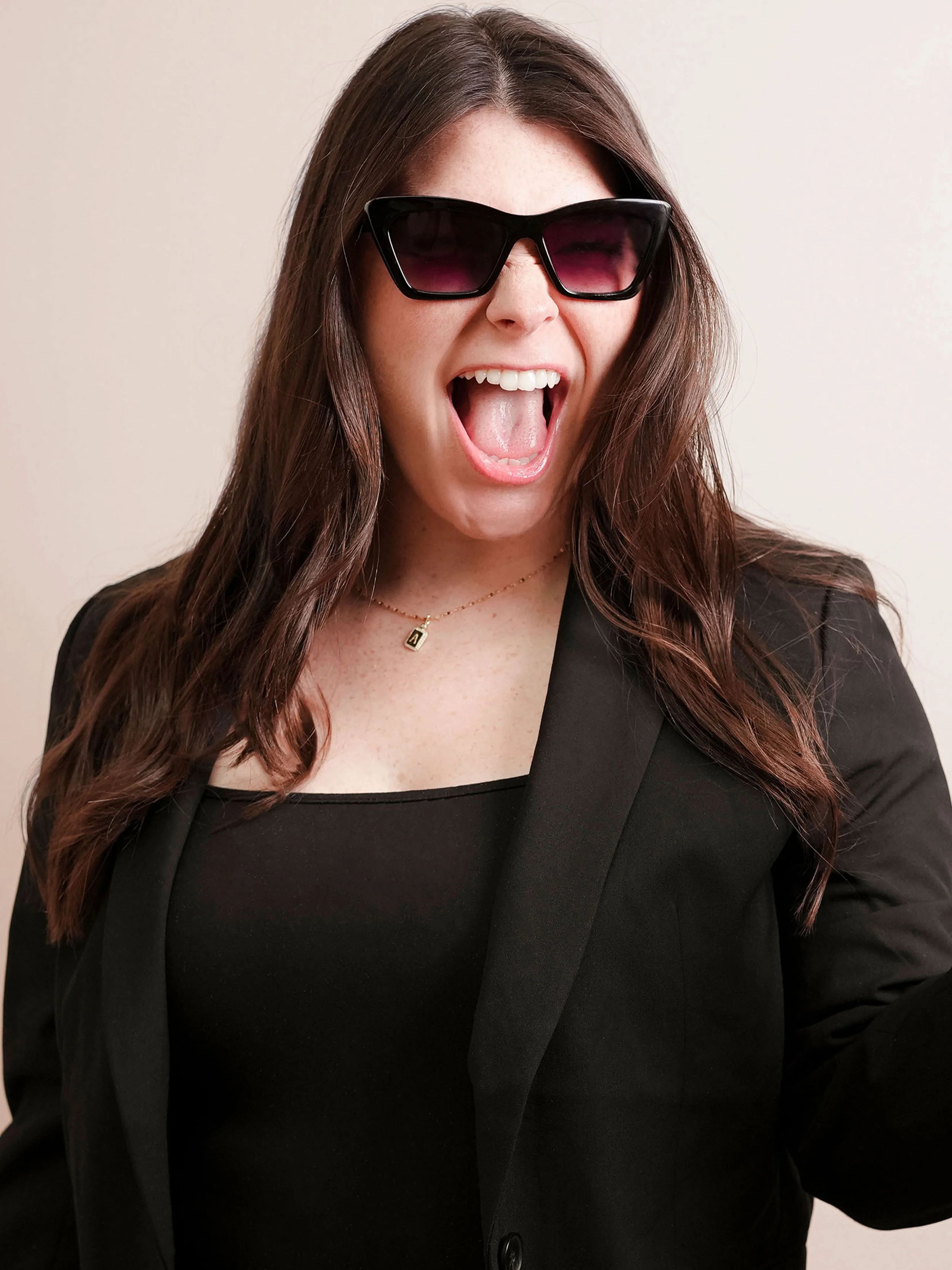 A woman with long dark wavy hair smiling and wearing a blue sweatshirt and jeans in a hair salon, holding a white purse with a gold handle.