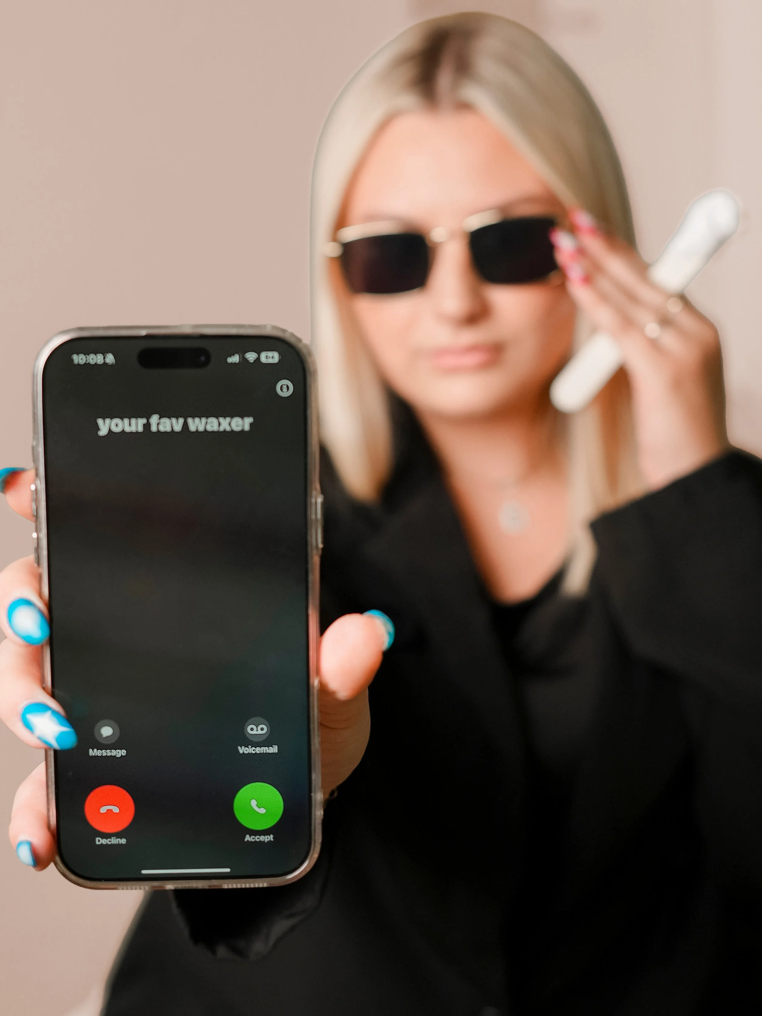 A young woman with blonde hair wearing a beige sweatshirt, sitting with her arms crossed, smiling at the camera in an indoor setting with wooden flooring and ceiling lights.