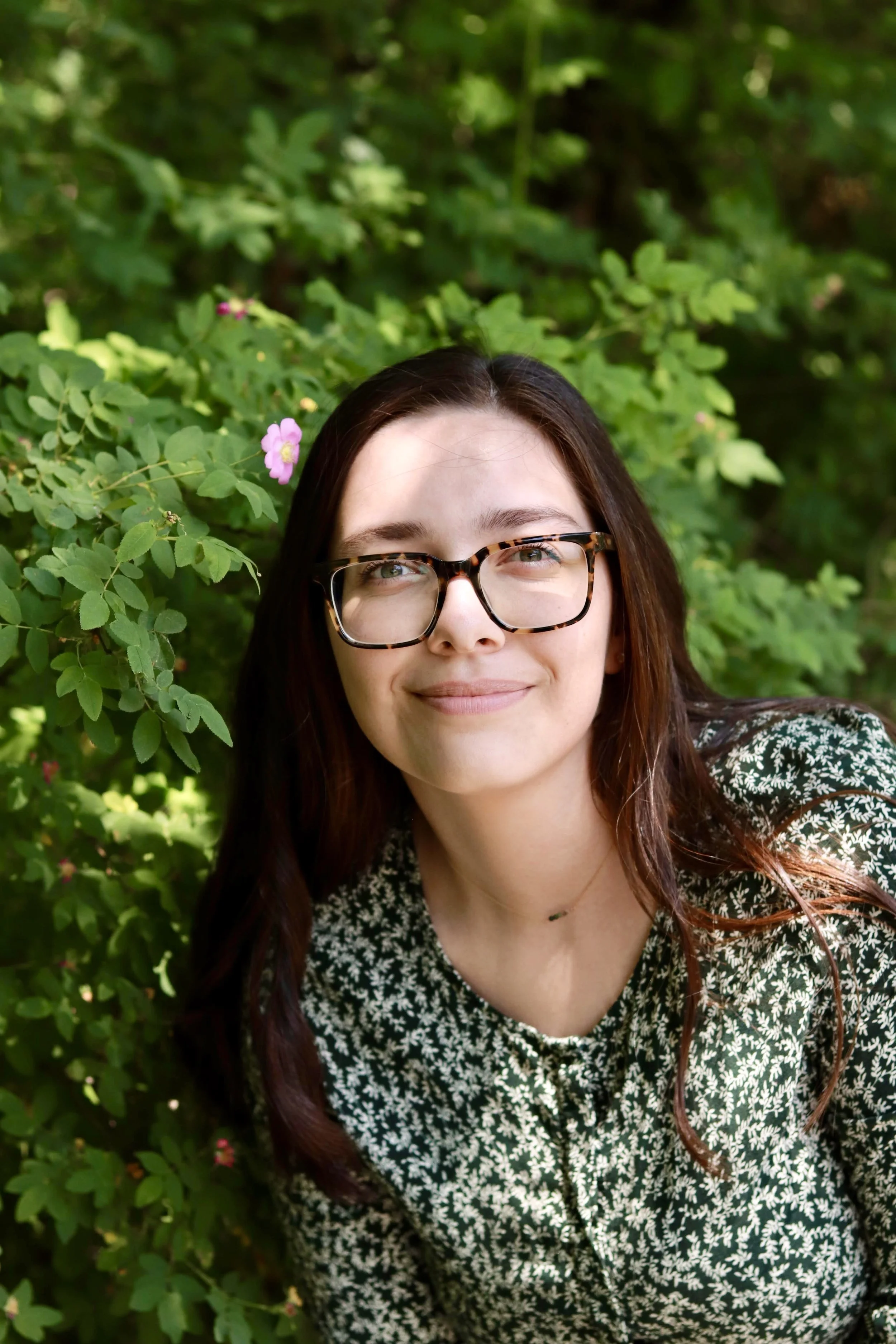 woman smiling at the camera in front of a bush