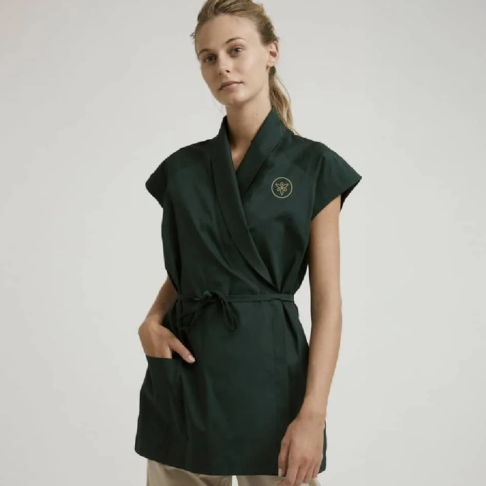 Woman wearing a dark wellness uniform with Tru Body logo, standing against a neutral background