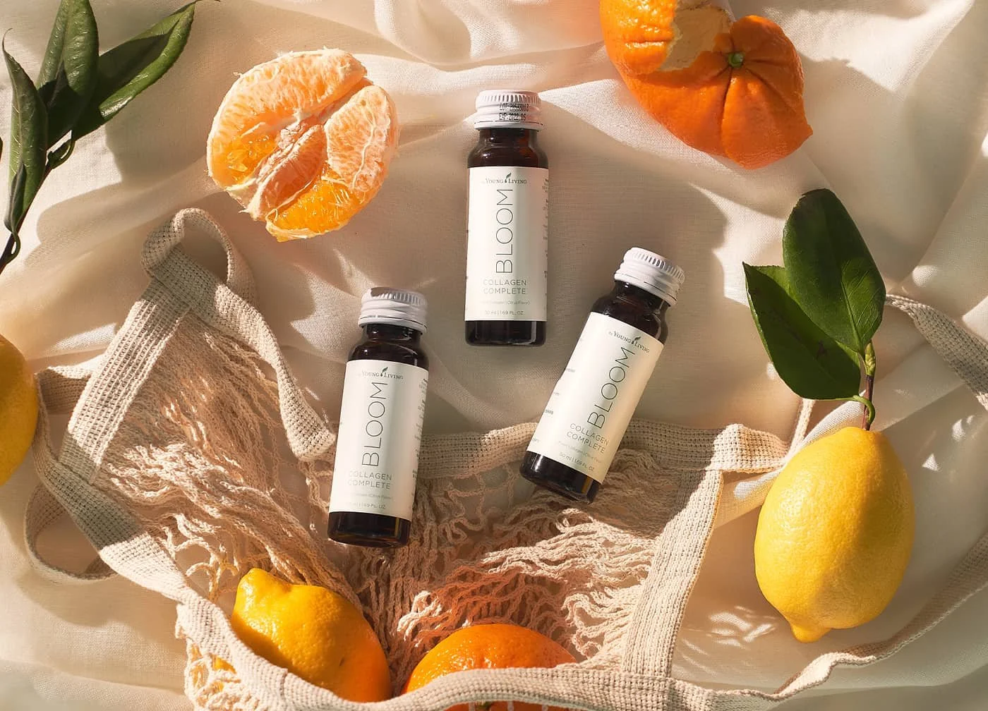 Flatlay of three Bloom collagen supplement bottles arranged with citrus fruits and a mesh bag