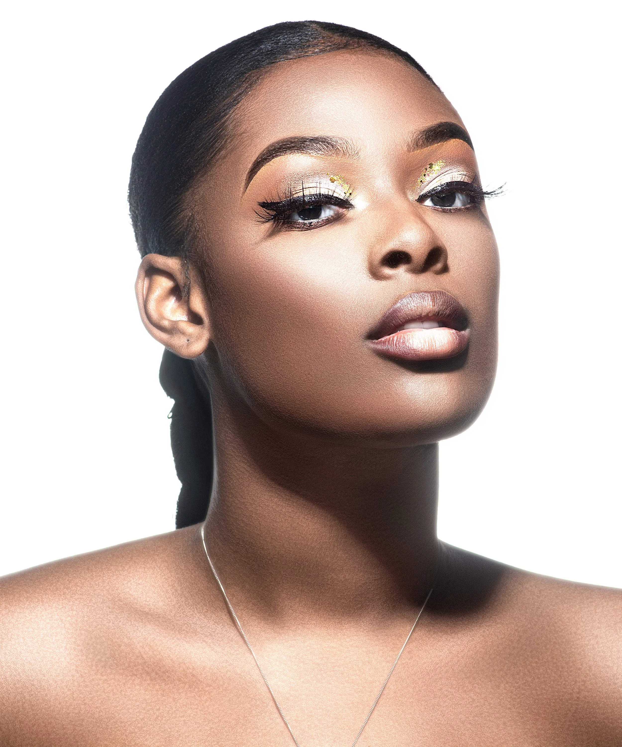 Close-up of a woman with smooth skin, short dark hair, and gold eyeshadow with glitter accents, wearing a thin silver necklace. Cleveland Photographer. Cleveland Portrait Photographer