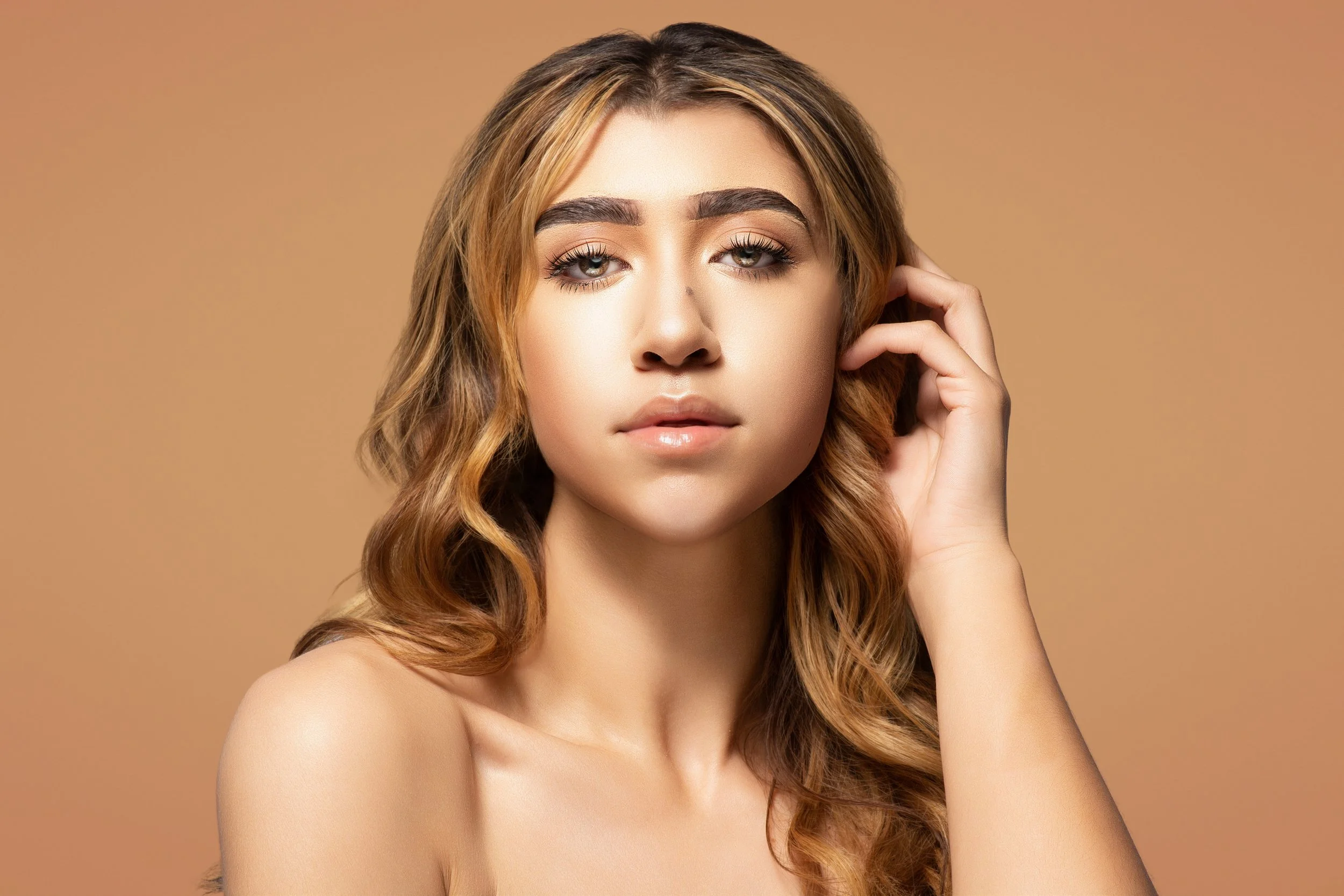 Close-up of a woman with long wavy hair, light makeup, and natural expression, touching her hair with her right hand. Cleveland Photographer. Cleveland Portrait Photographer