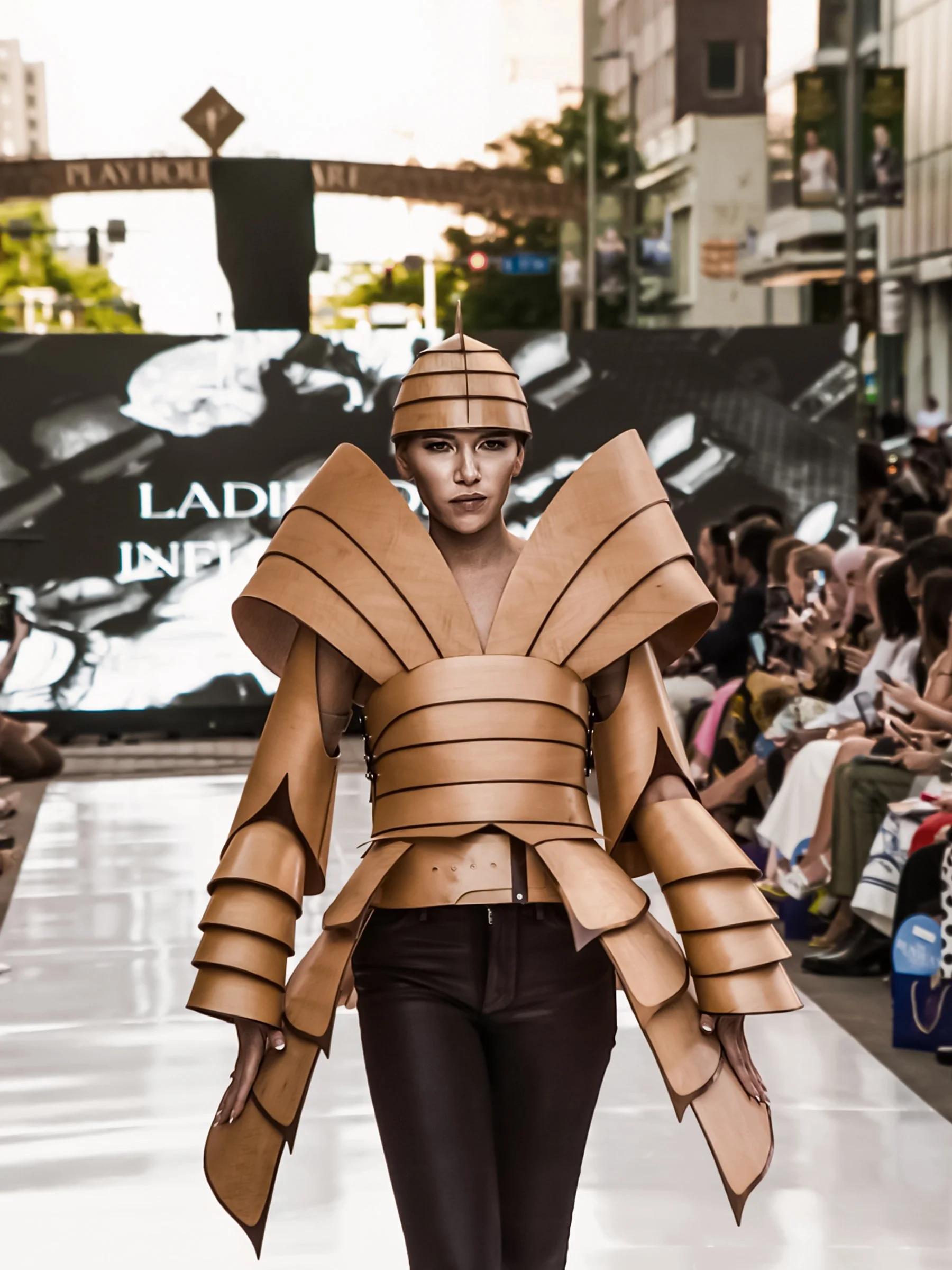 Female model walking down runway in a futuristic beige and brown wooden armor-inspired outfit with geometric shapes at a fashion show. Cleveland Photographer. Cleveland Portrait. Fashion Talks
