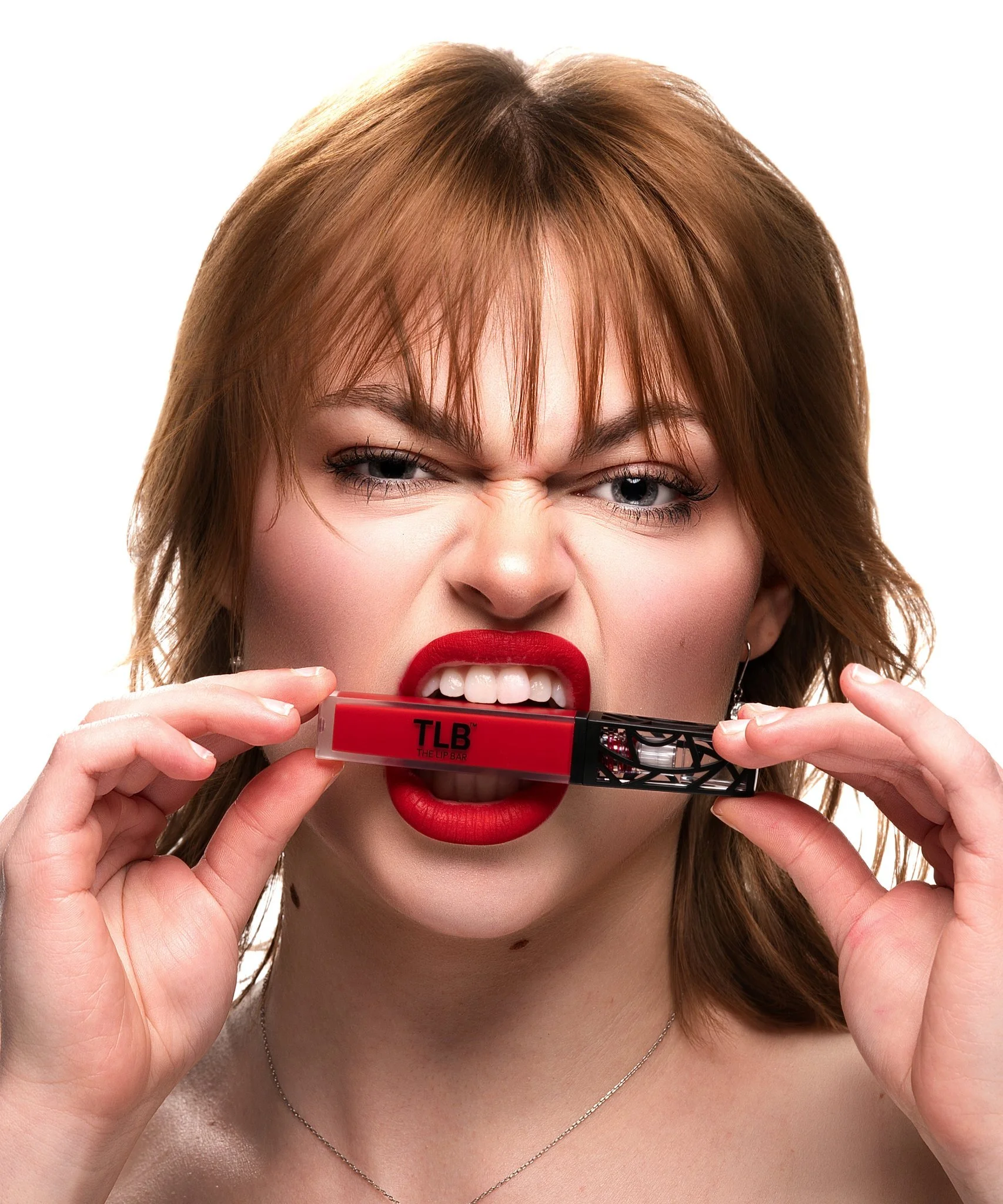 Close-up of a woman with reddish-brown hair and red lipstick, holding a red lip balm labeled "TLB" near her lips, making a playful expression. Cleveland Photographer. Cleveland Portrait Photographer