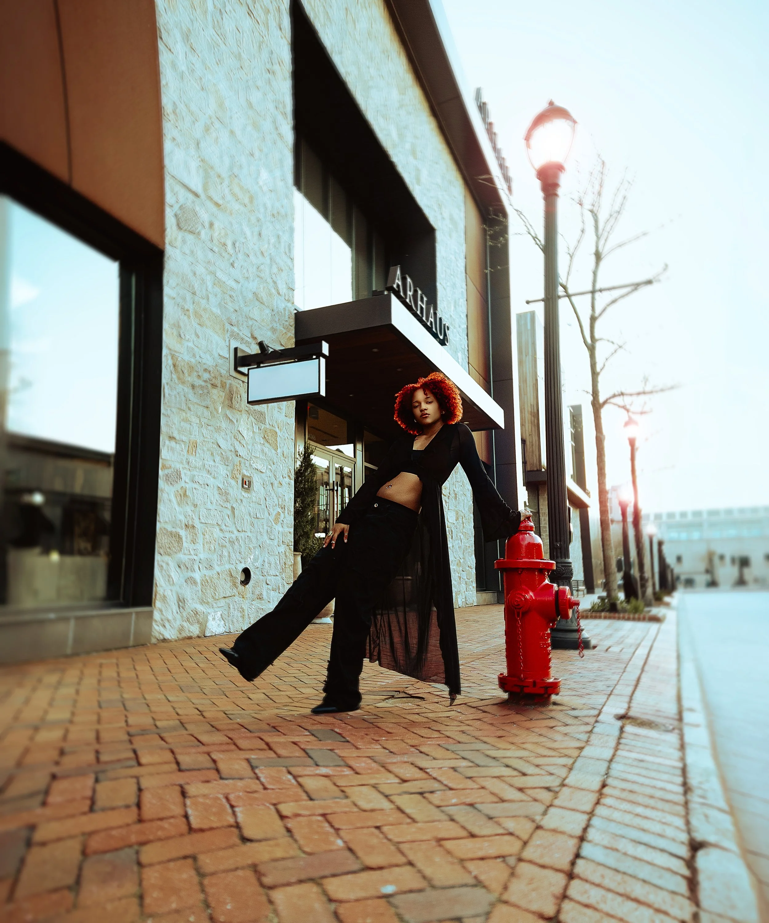 A woman with curly red hair wearing black clothing standing on a brick sidewalk outside a modern building with a sign that reads 'ARTHAUS.' Cleveland Photographer. Cleveland Portrait Photographer, Legacy Village