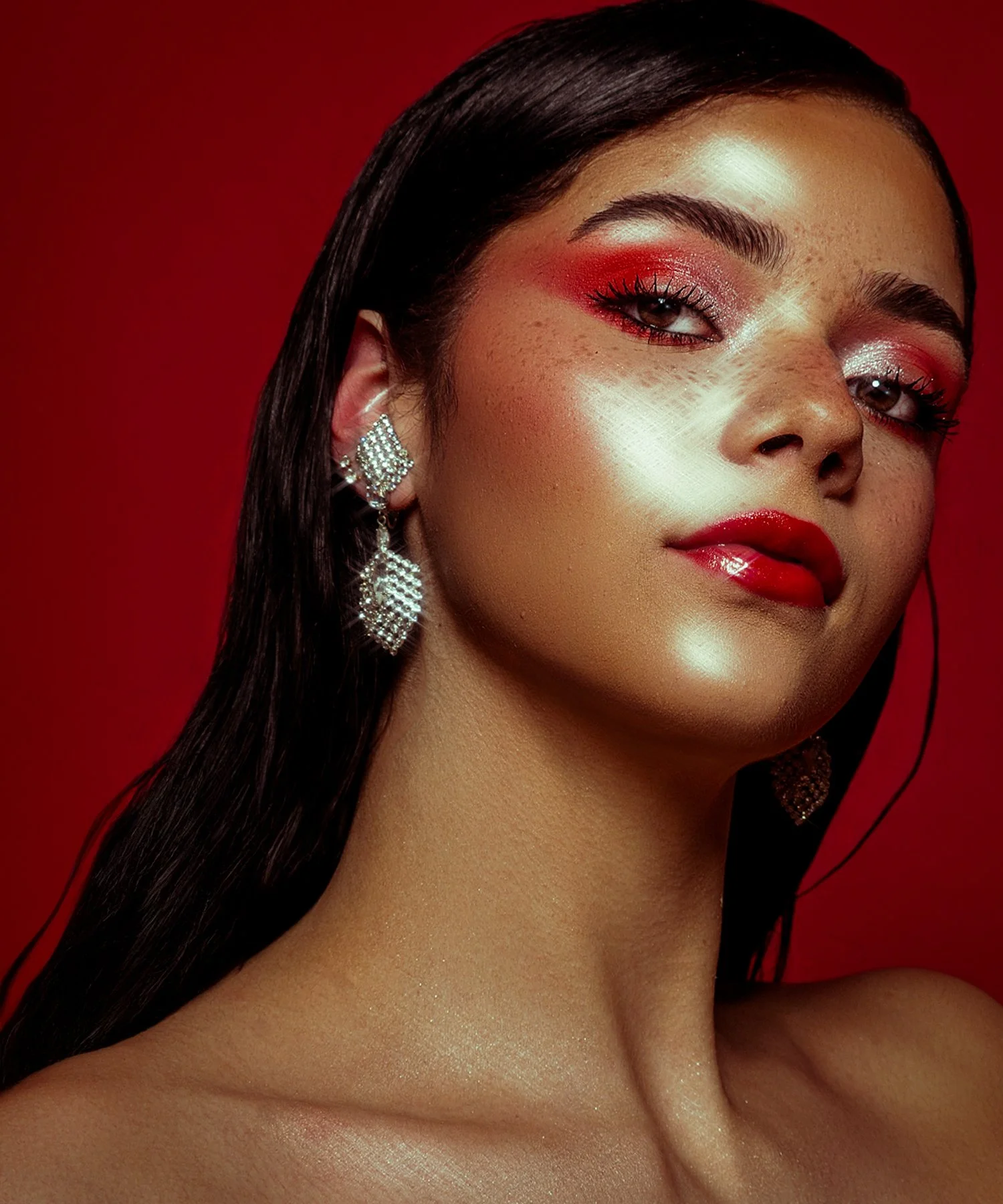Close-up of a woman with long, dark hair, wearing silver earrings, with red makeup on her eyelids and lips, and a red background. Cleveland Photographer. Cleveland Portrait Photographer