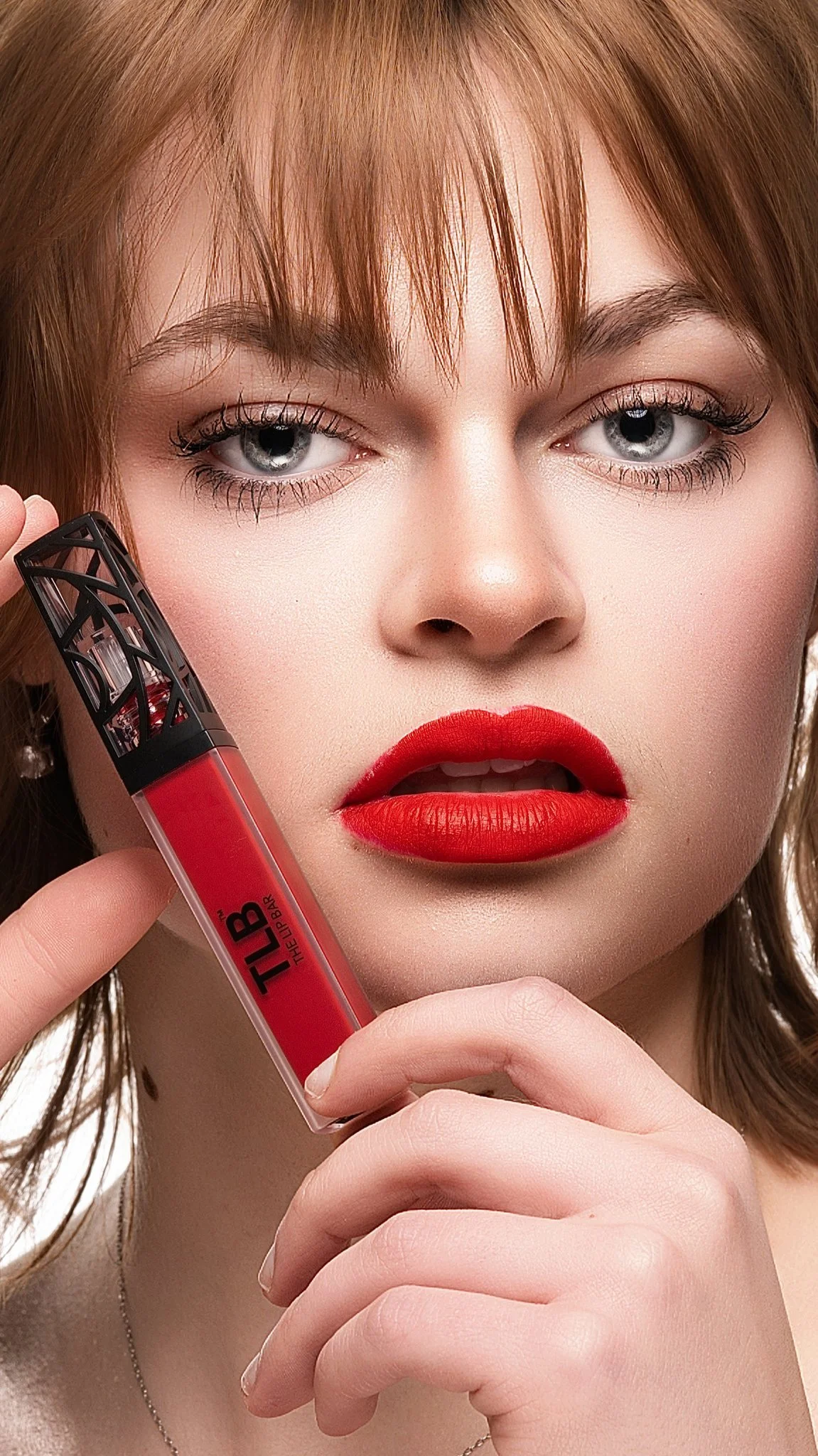 Close-up of a woman with red lipstick, holding a tube of liquid lipstick near her face. Cleveland Photographer. Cleveland Portrait Photographer