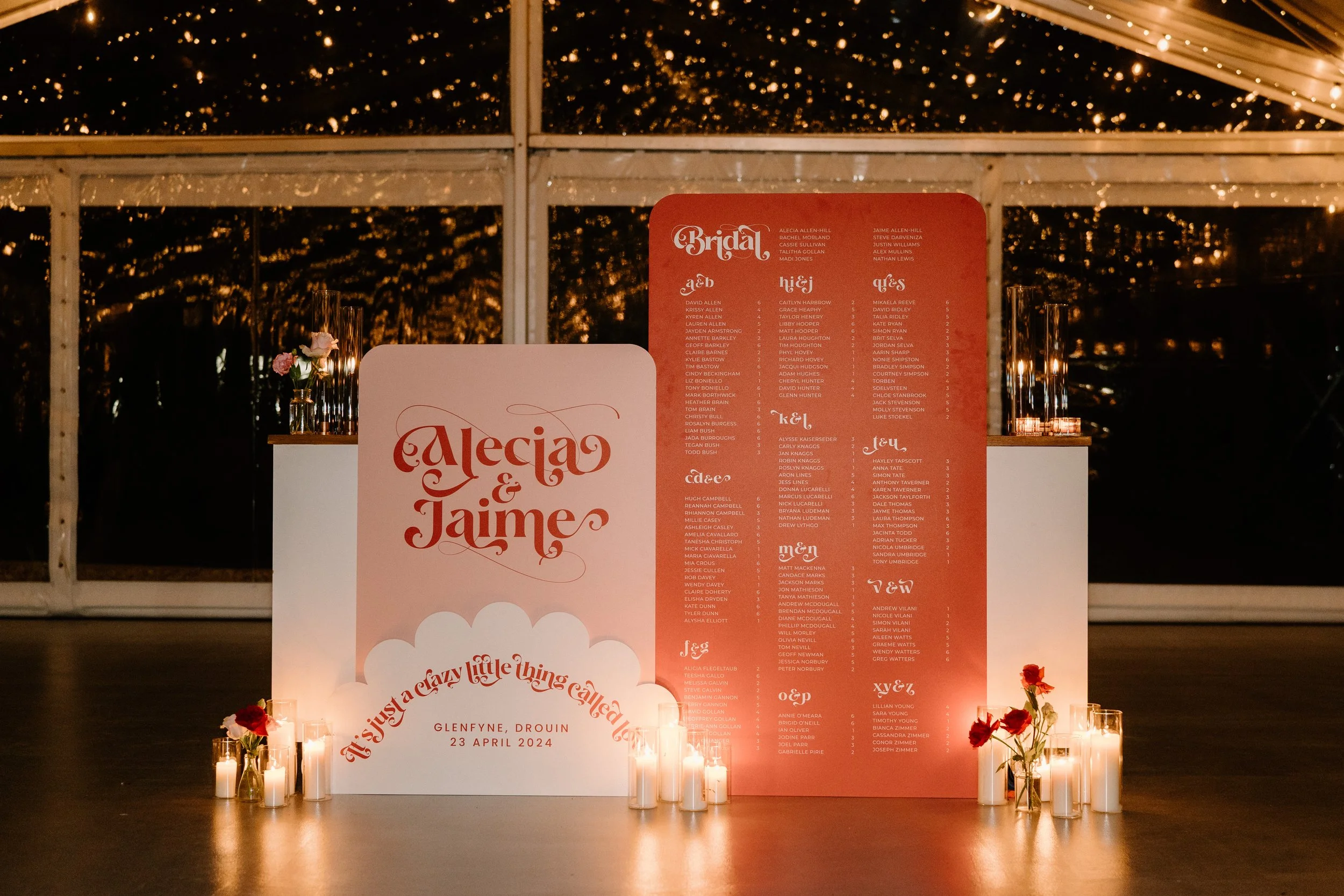 Wedding seating chart display with Danse and Alecia & Jaime, decorated with candles and flowers, inside a tent at night.
