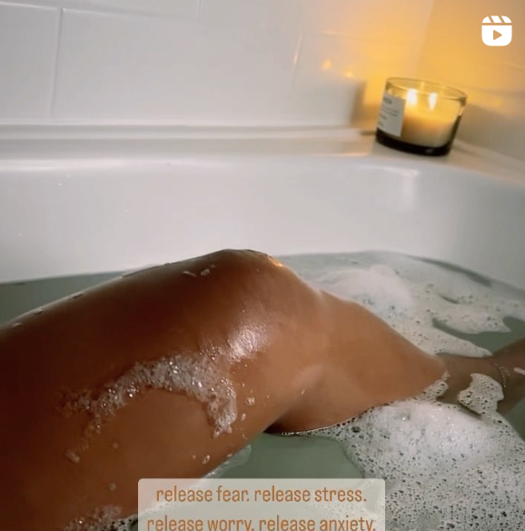 Person relaxing in a bathtub with a lit candle nearby.