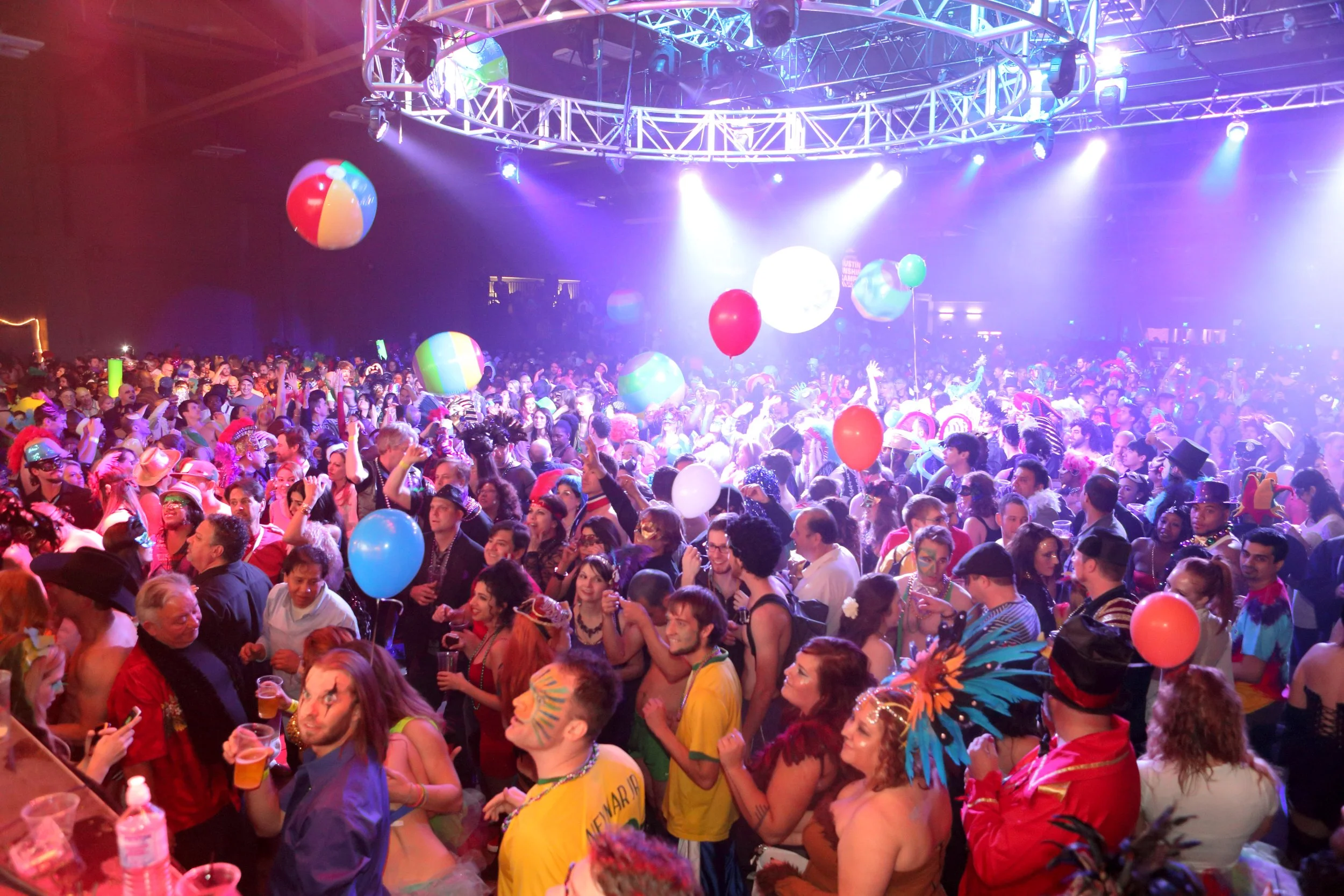 Crowd of people at Carnaval Austin with balloons, festive clothing, and colorful lighting. Happening February 7, 2026!