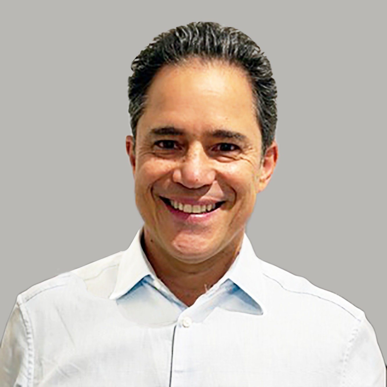 A smiling man with dark hair, dressed in a light-colored button-up shirt, against a gray background.