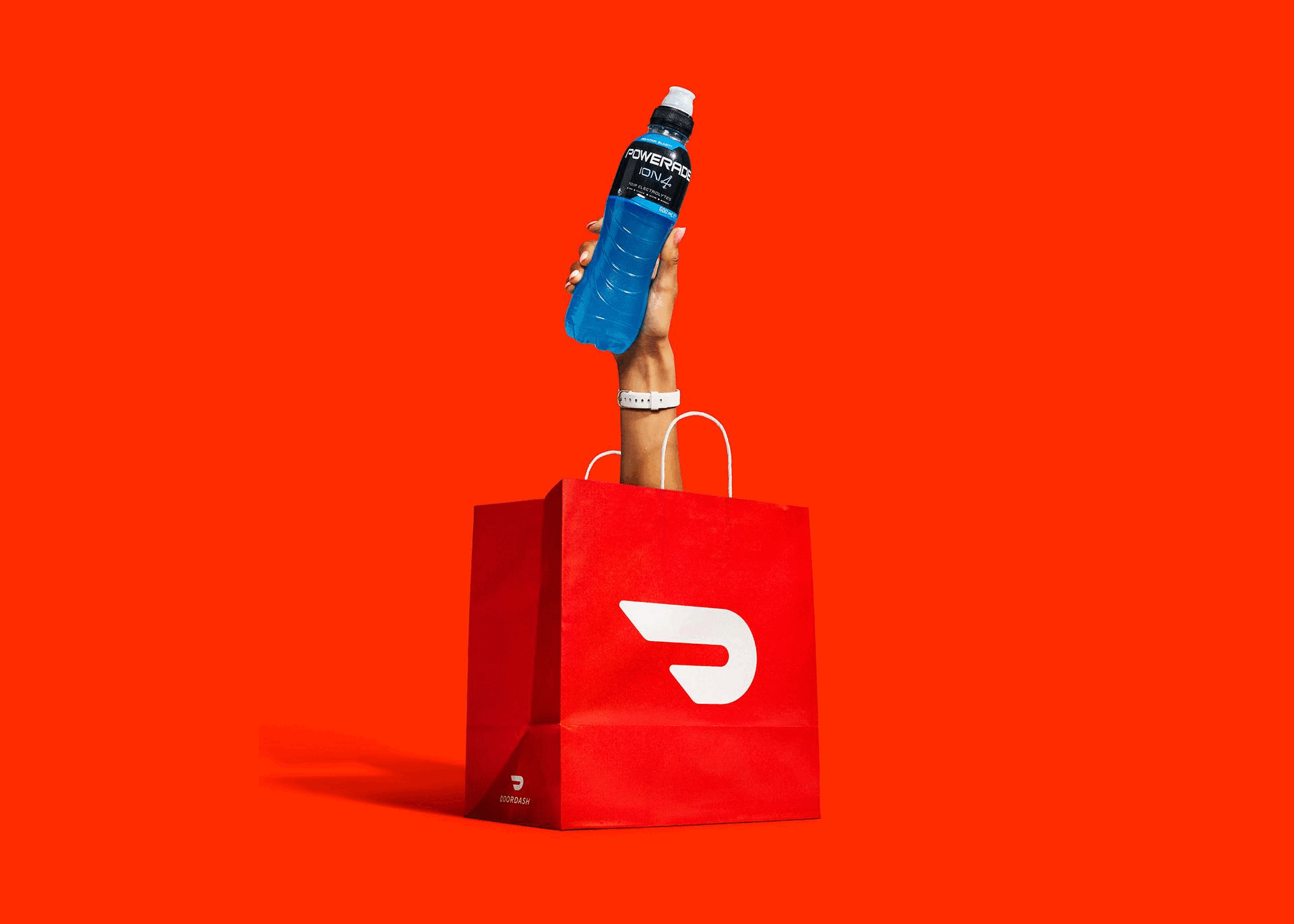 A hand holding a blue sports drink bottle emerging from a red shopping bag with a white logo on a red background.