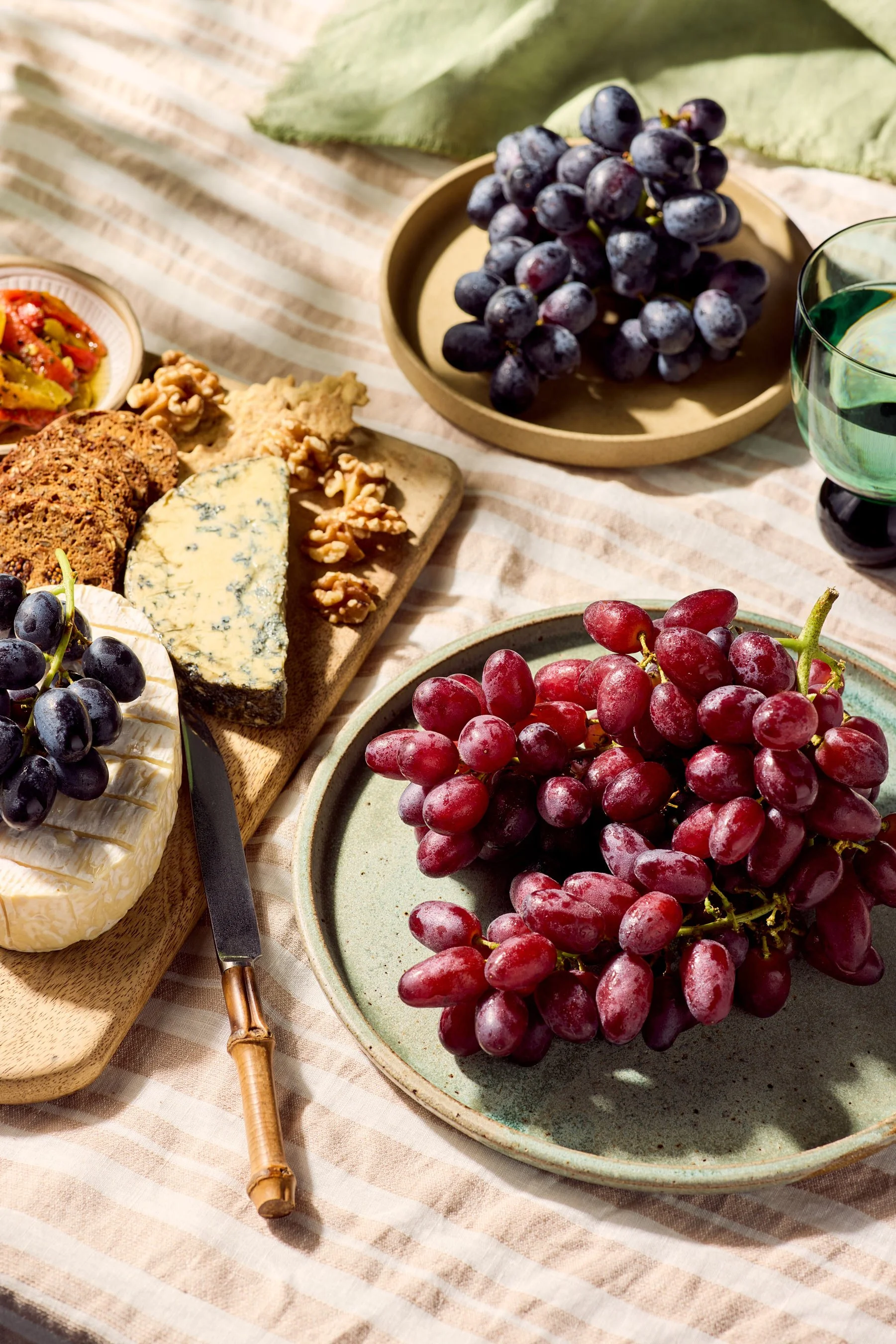 Close-up of a cheese platter with grapes, nuts, and crackers on a table with a striped cloth.