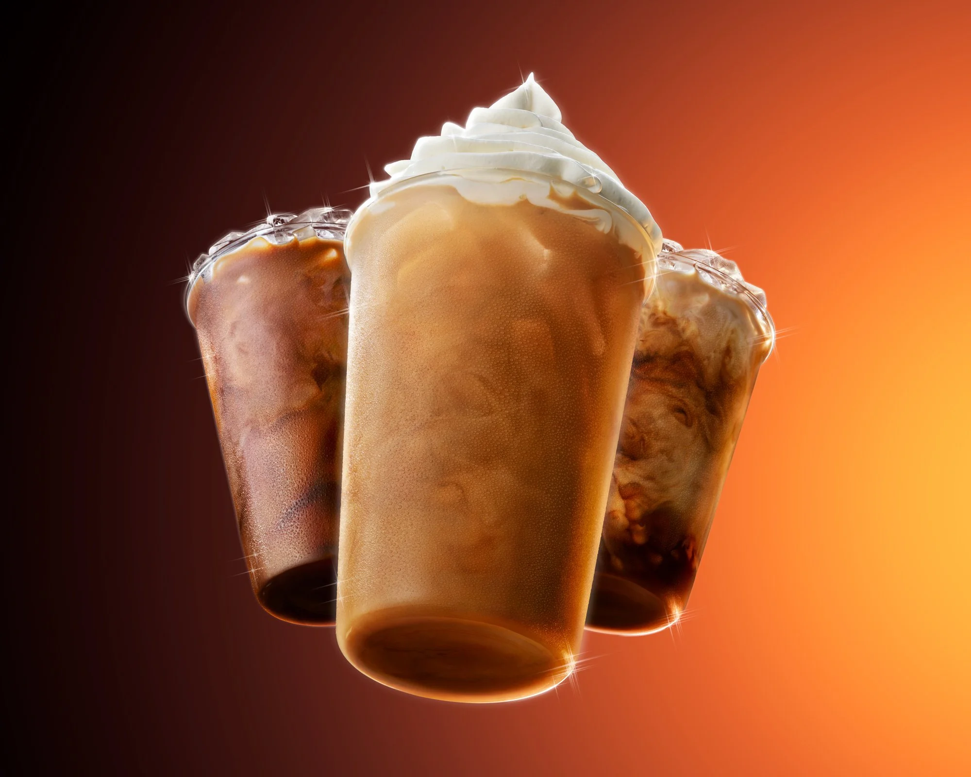 Three iced coffee drinks with whipped cream and caramel, against an orange background with a gradient effect.