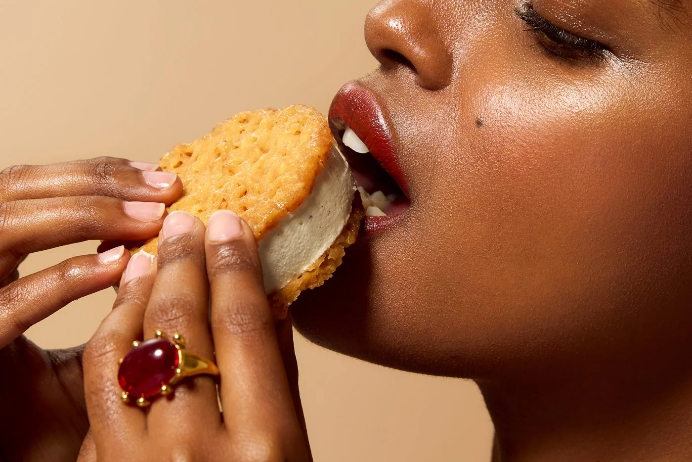 Close-up of a woman with dark skin and makeup, biting into a snack cake or cookie.