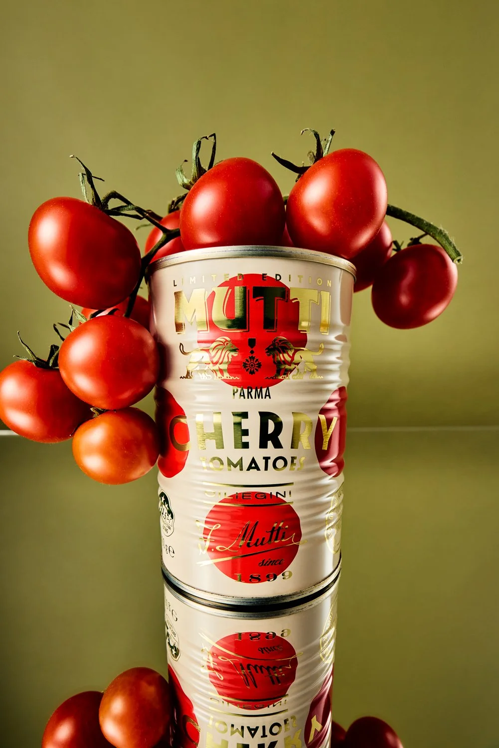 Bunch of cherry tomatoes resting on top of a Mutti Cherry Tomato can with a green background. shot on a wide angle lens and mirrored base.