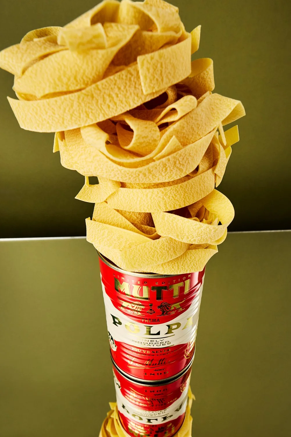 Layered uncooked pasta noodles stacked vertically on a red and white Mutti can of tomatoes. shot on a wide angle lens