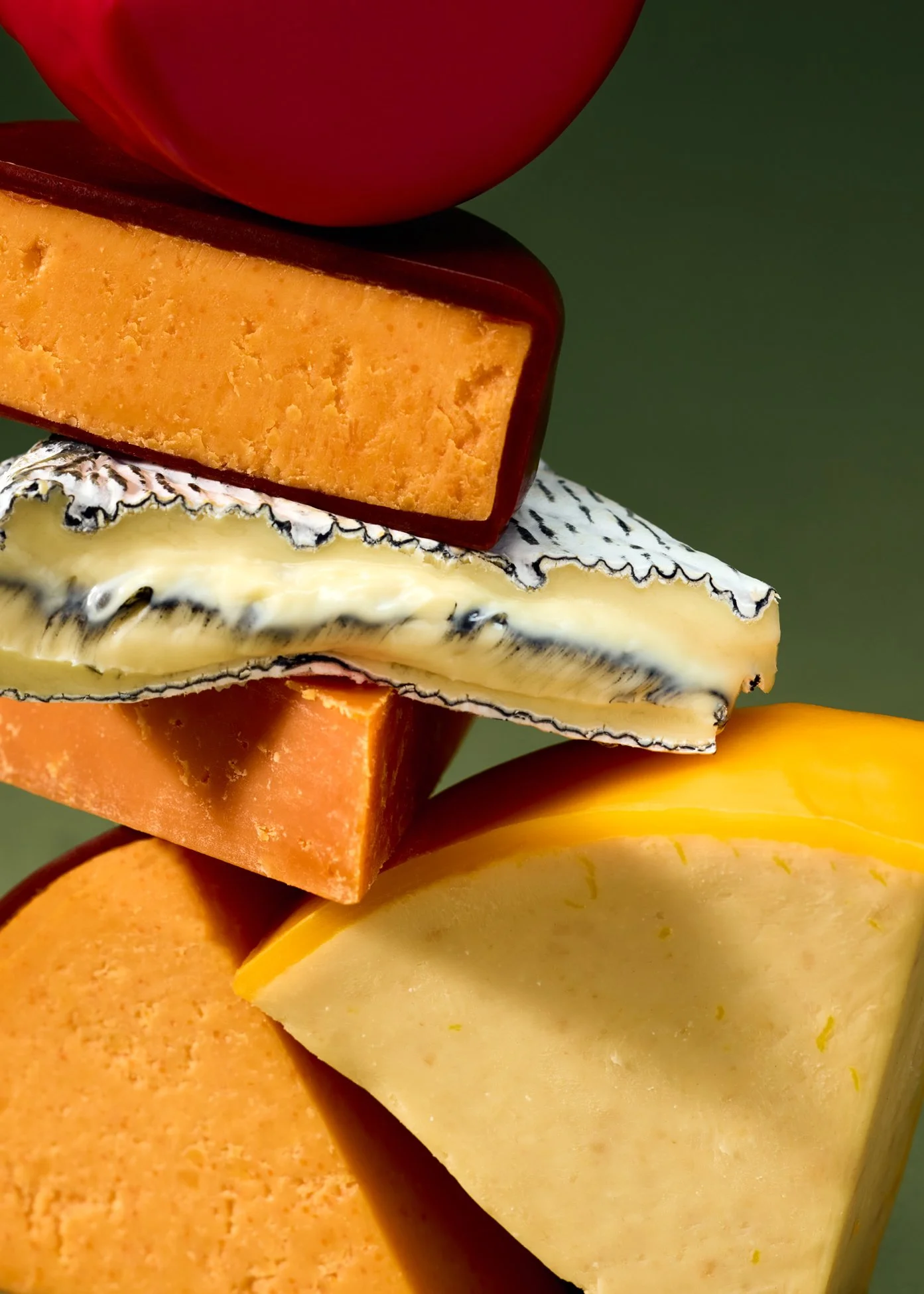 Close-up of a vertical stack of assorted cheese slices with different textures and colors on a green background.