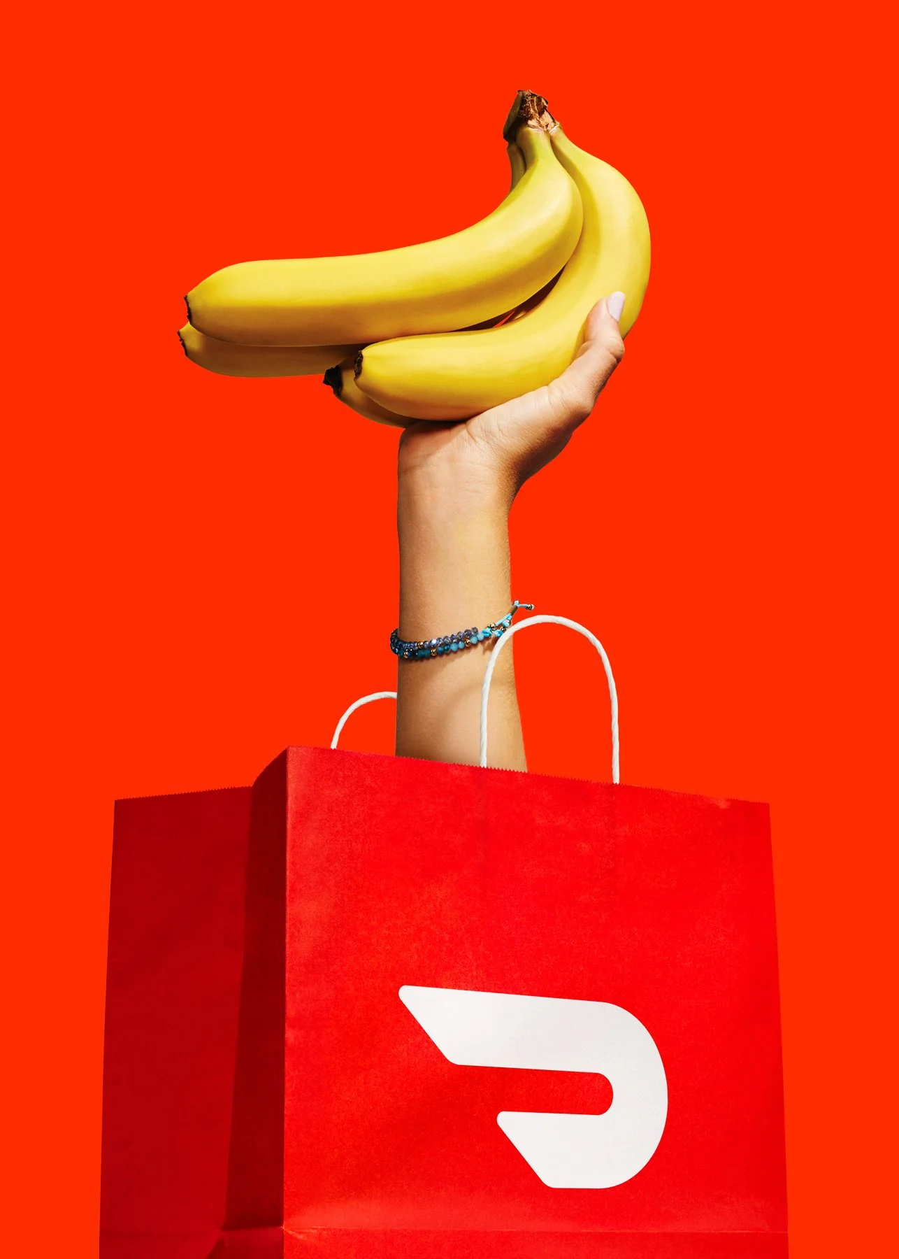 Doordash advertising campaign ''smash it''.  A hand holding three bananas above coming out of a shopping bag with a white DoorDash logo against a red background.