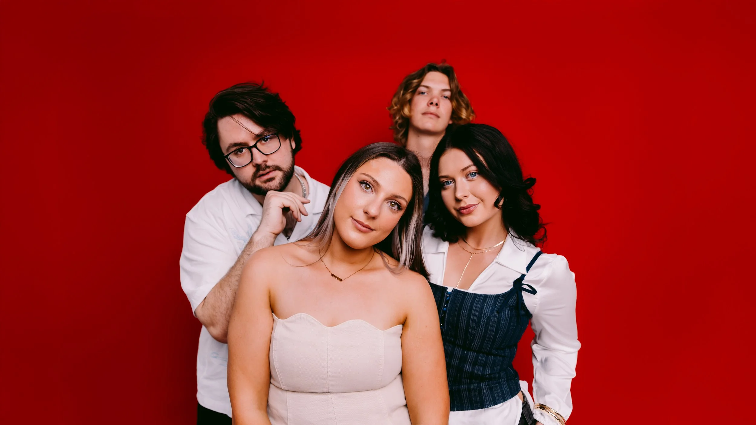 Group of five young adults posing against a solid red background.