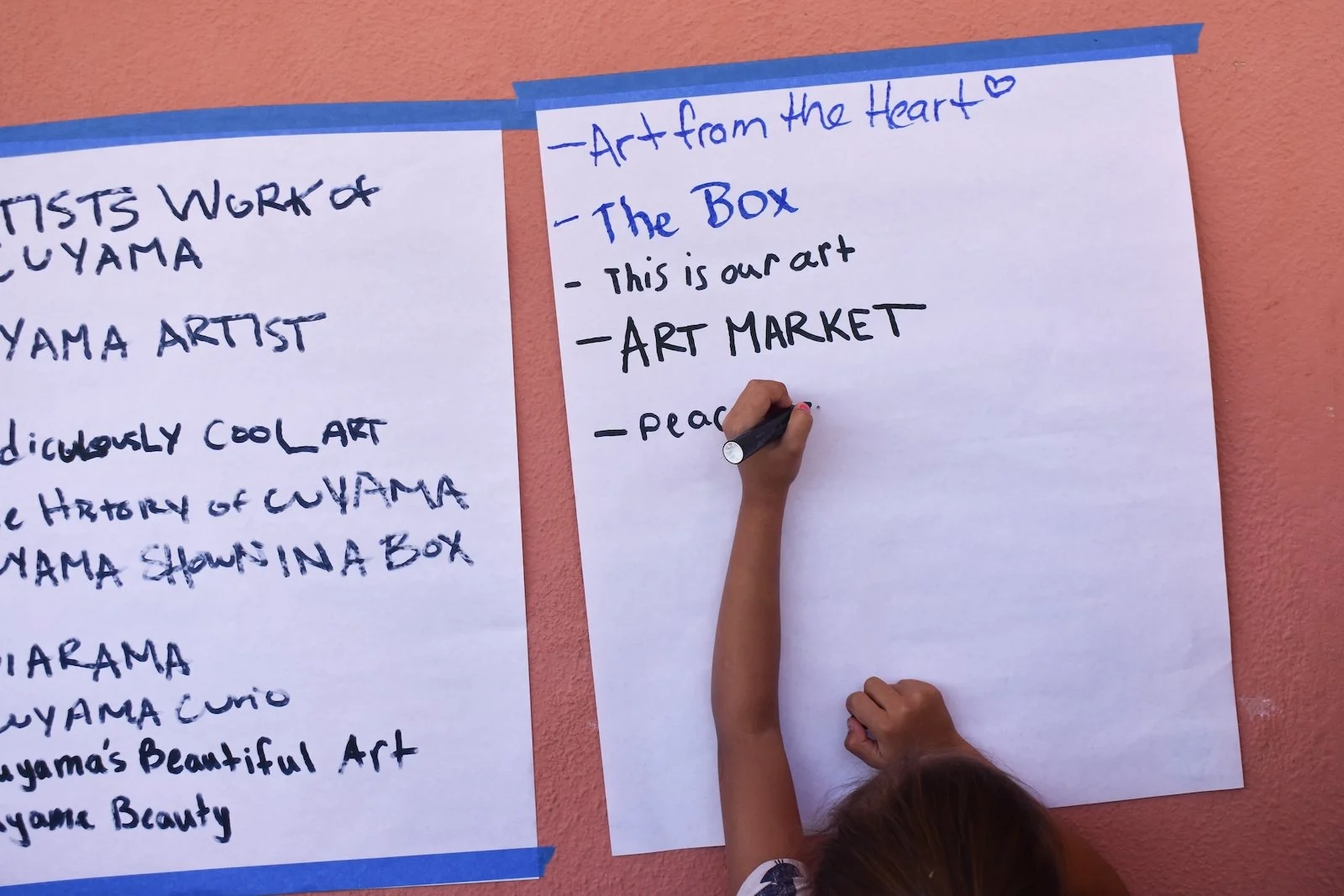 A young artist adds their contribution to the suggestions for the community art gallery at the "Cuyama Cartonera" exhibition. During her residency, Mayela refurbished the old National Forest Service display case connected to the town market to create