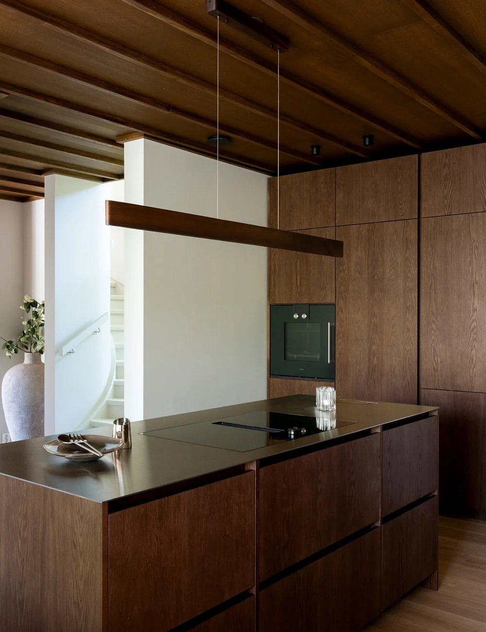Køkkenø i mørk eg med bordplade i rustfrit stål og højskabe i et hjem inspireret af Mid-Century Modern.