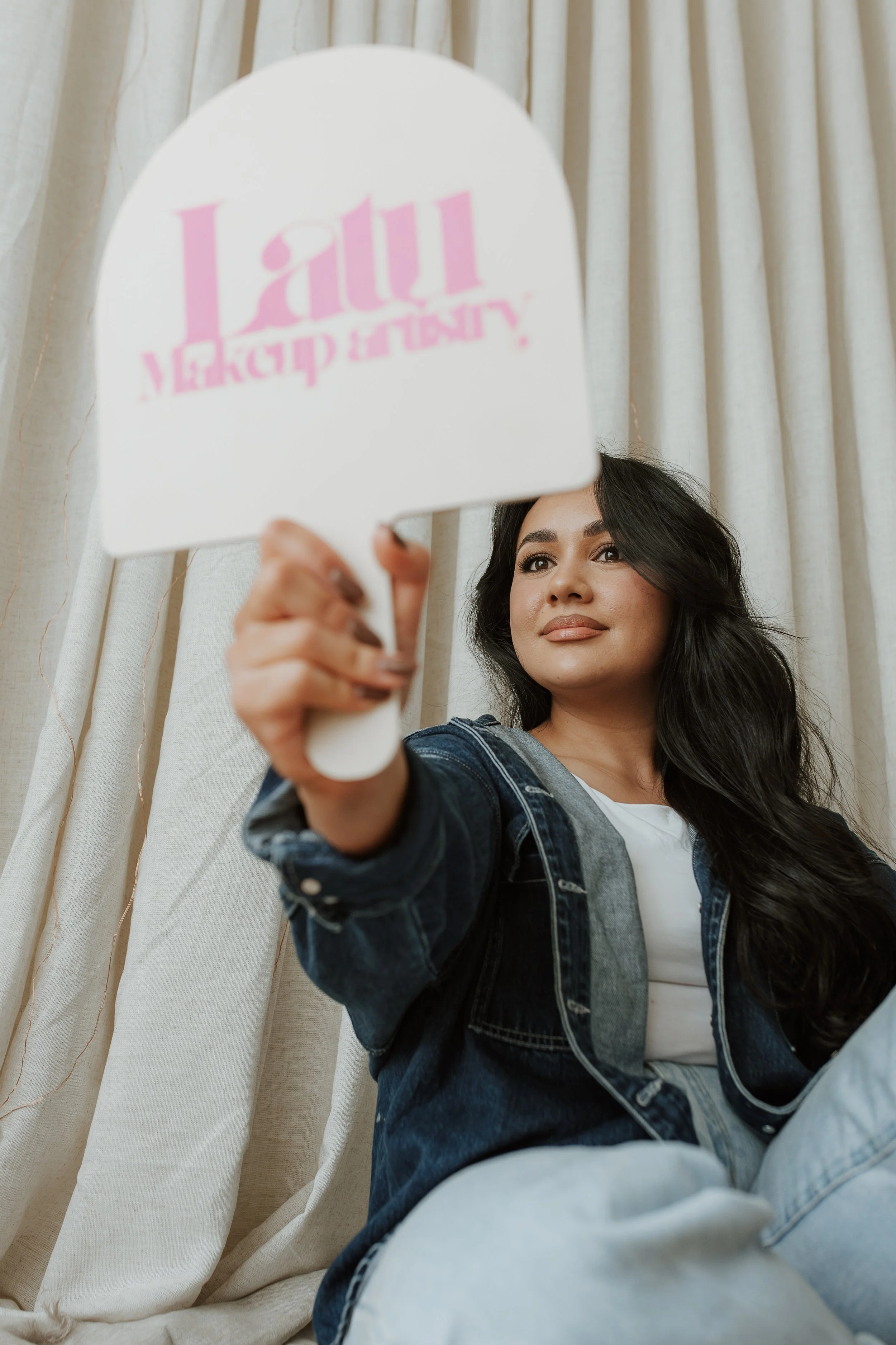 A woman smiling at herself looking into a makeup mirror with her own business branding on it