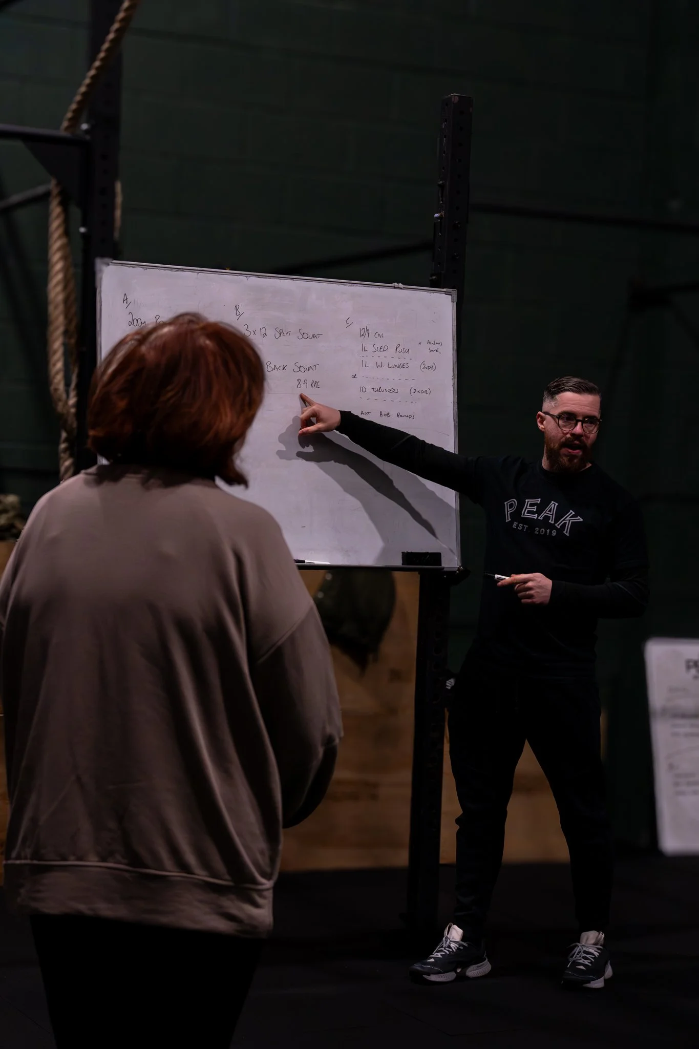A coach leading a fitness session showing what is programmed for the clients. He is instructing them on the movements and techniques that have been planned for them. These run in the Denton and Hyde area.