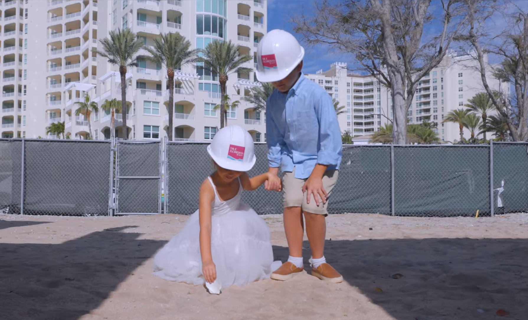 young boy and girl wearing hardhats placing a shell in the sand on the construction site of the ocean front property