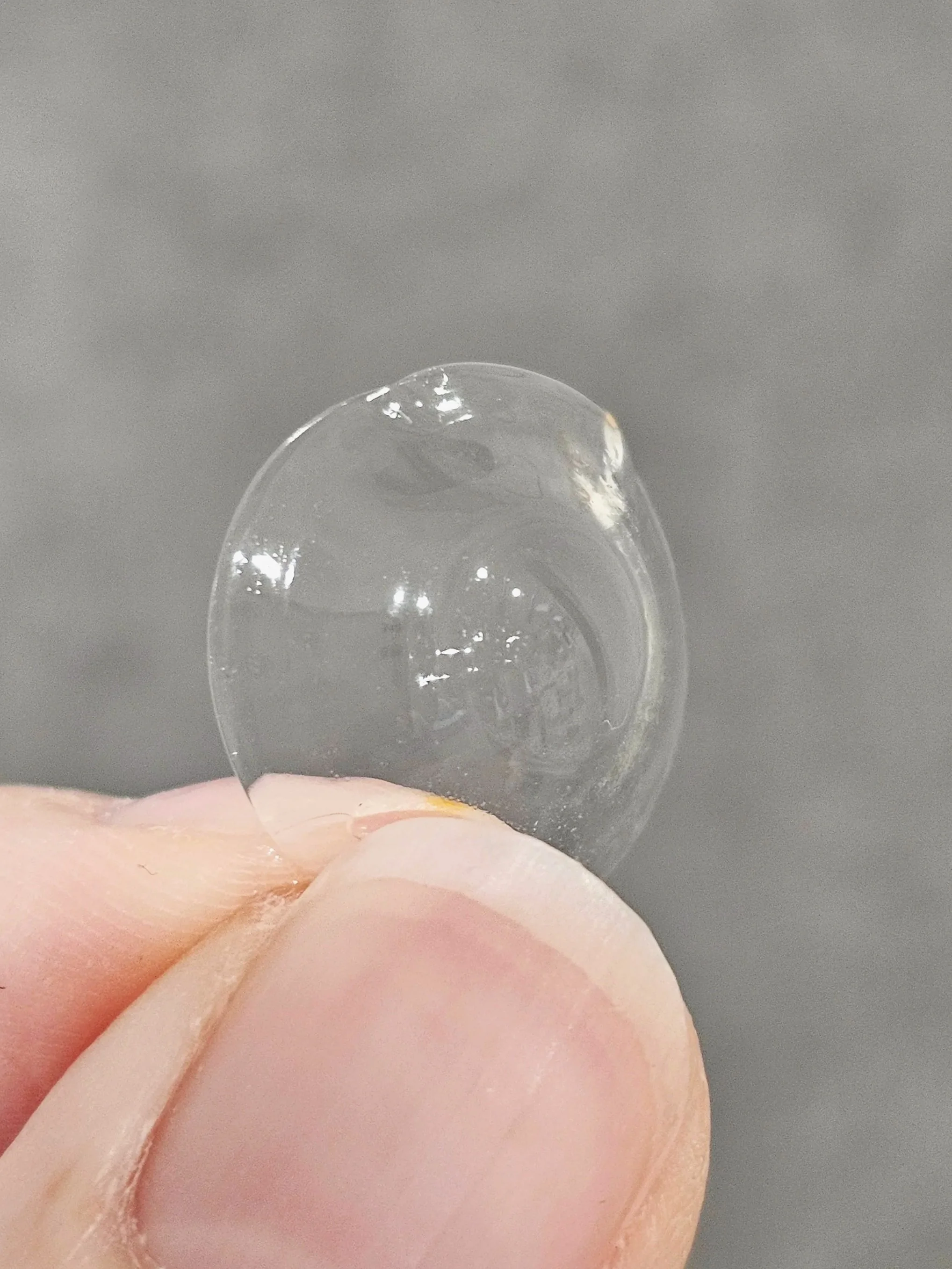 Close-up of a person's thumb and index finger holding an Eyeprint Pro contact lens with a very irregular customised profile.