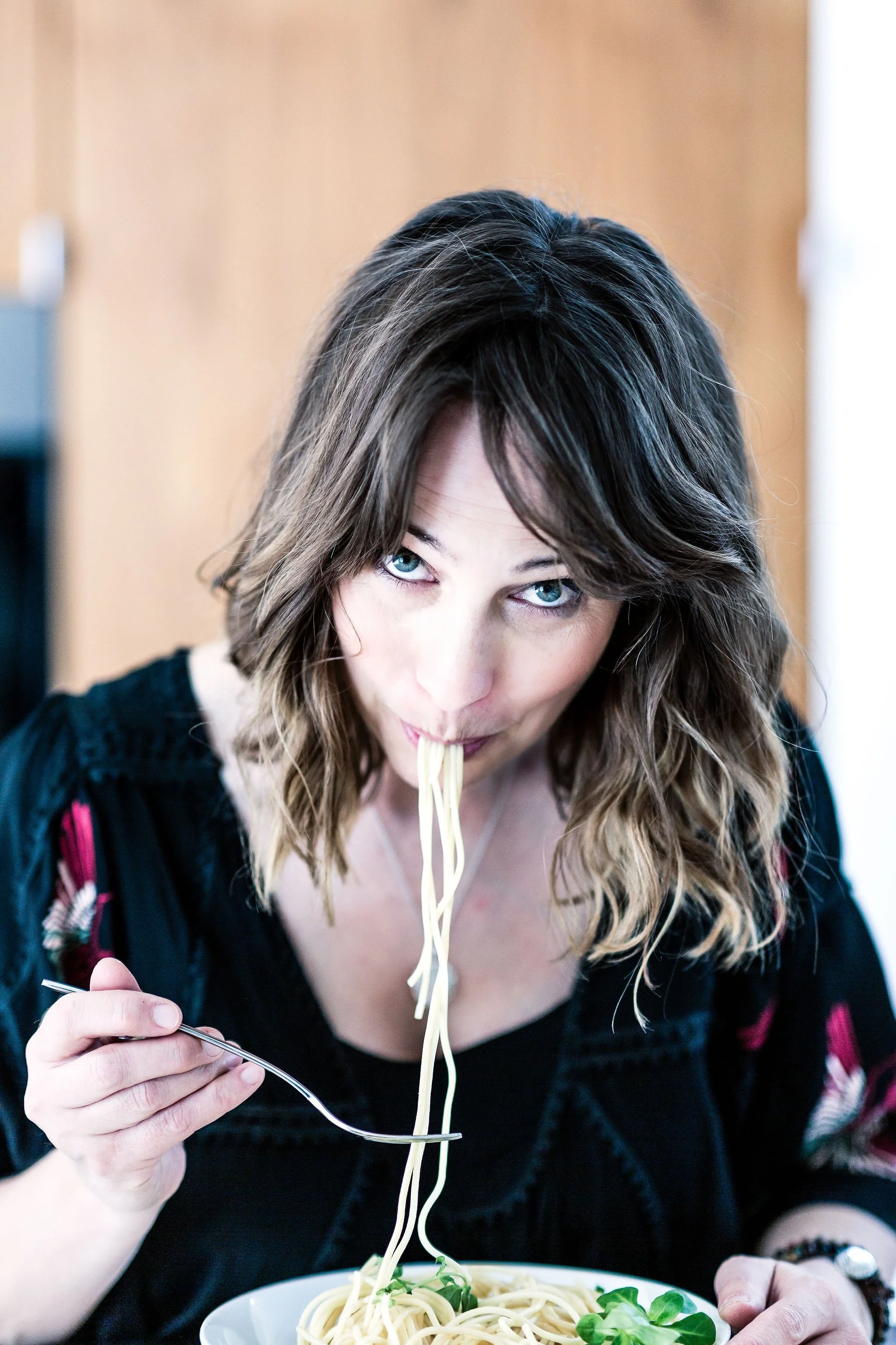 A woman with shoulder-length hair tasting spaghetti with a fork.