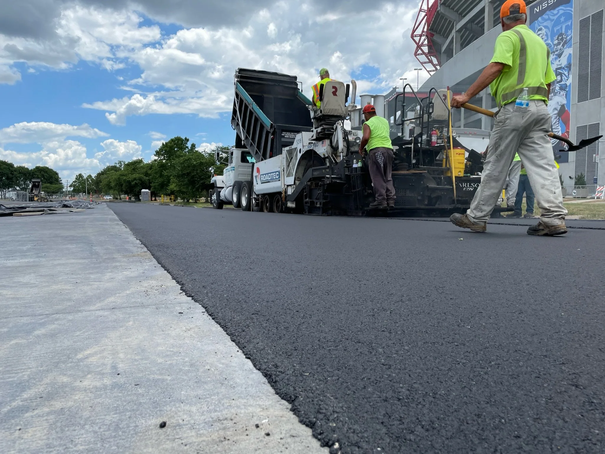 An image of the transition between the asphalt roadway and the concrete roadway for the Music City Grand Prix, Image shows a dump truck and a roadtec paver