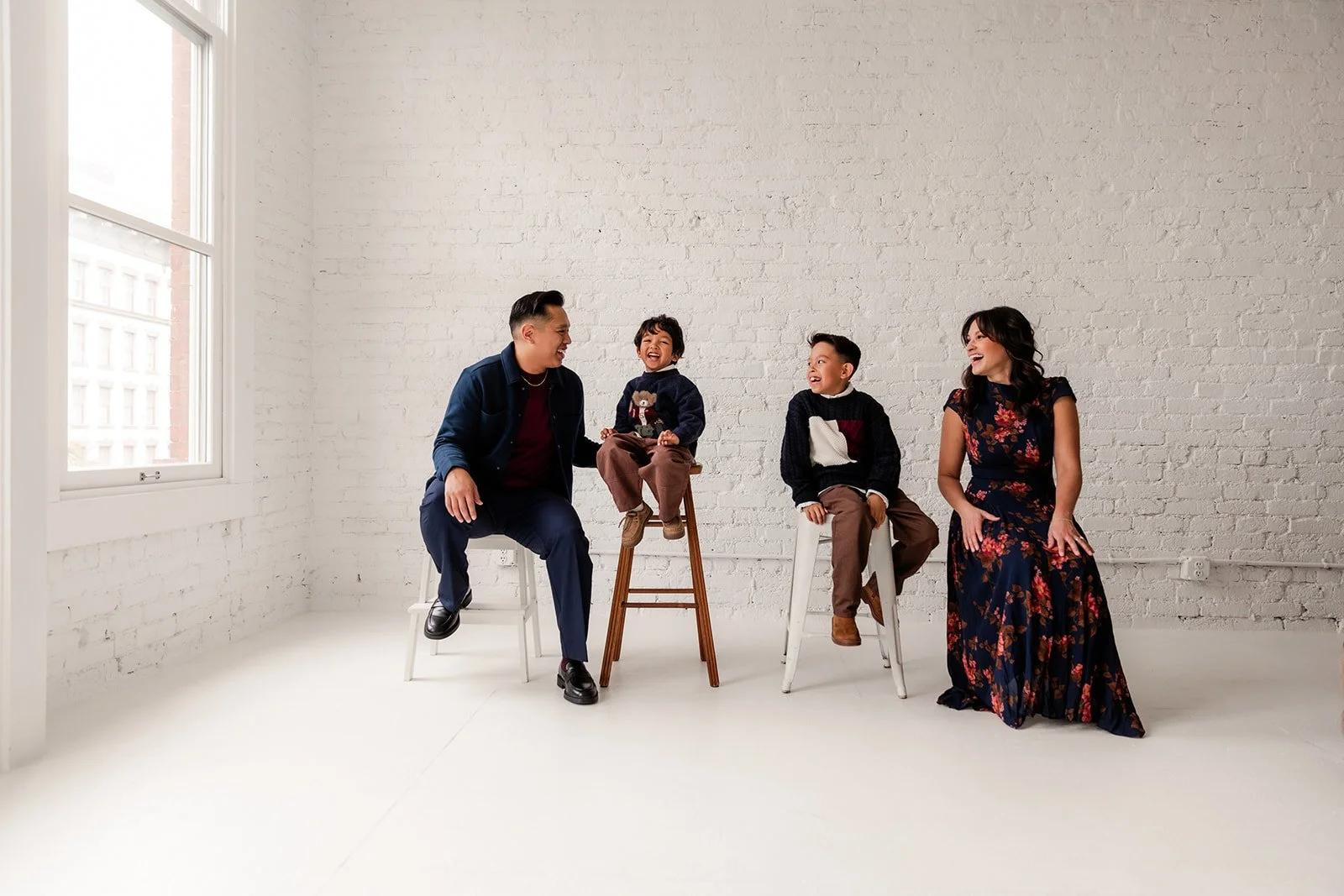 Family of four sit on a stools at a natural light studio
