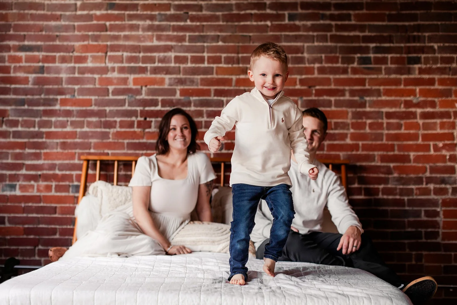 Little boy jumps on a bed while parents watch and smile