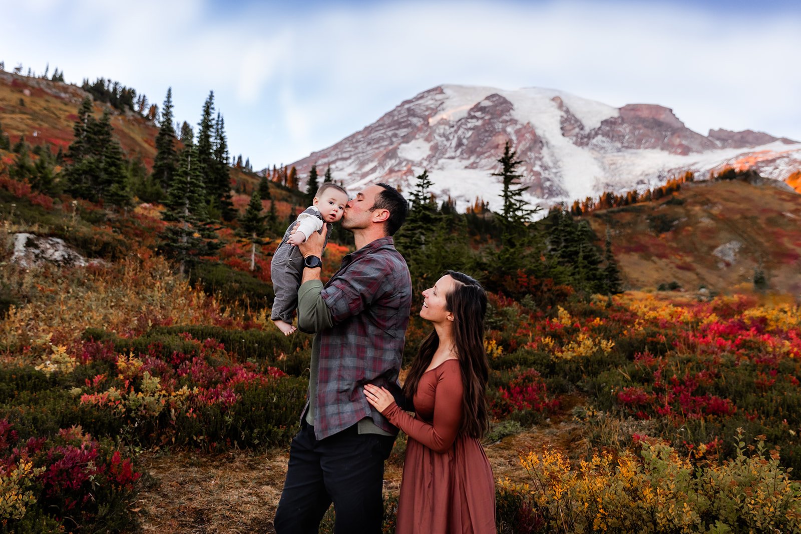 Dad kisses baby while mom looks on with Mt. Rainier in background