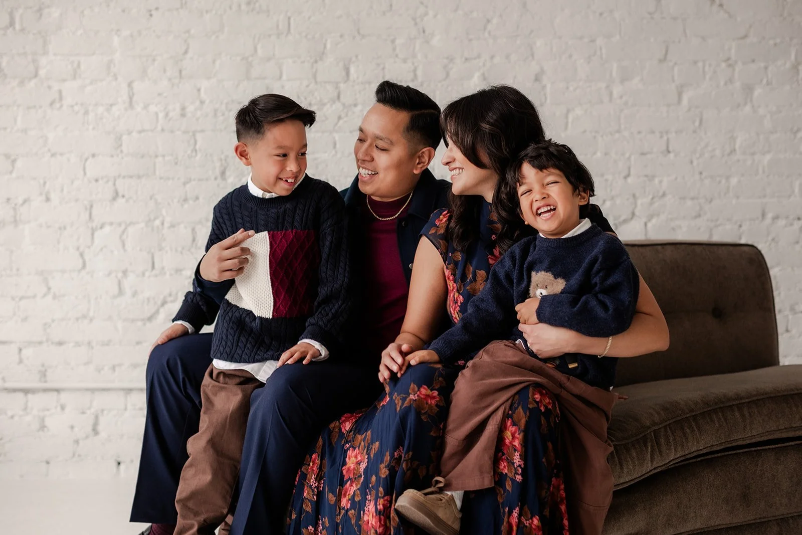 Family of 4 laughs together in a white brick wall studio