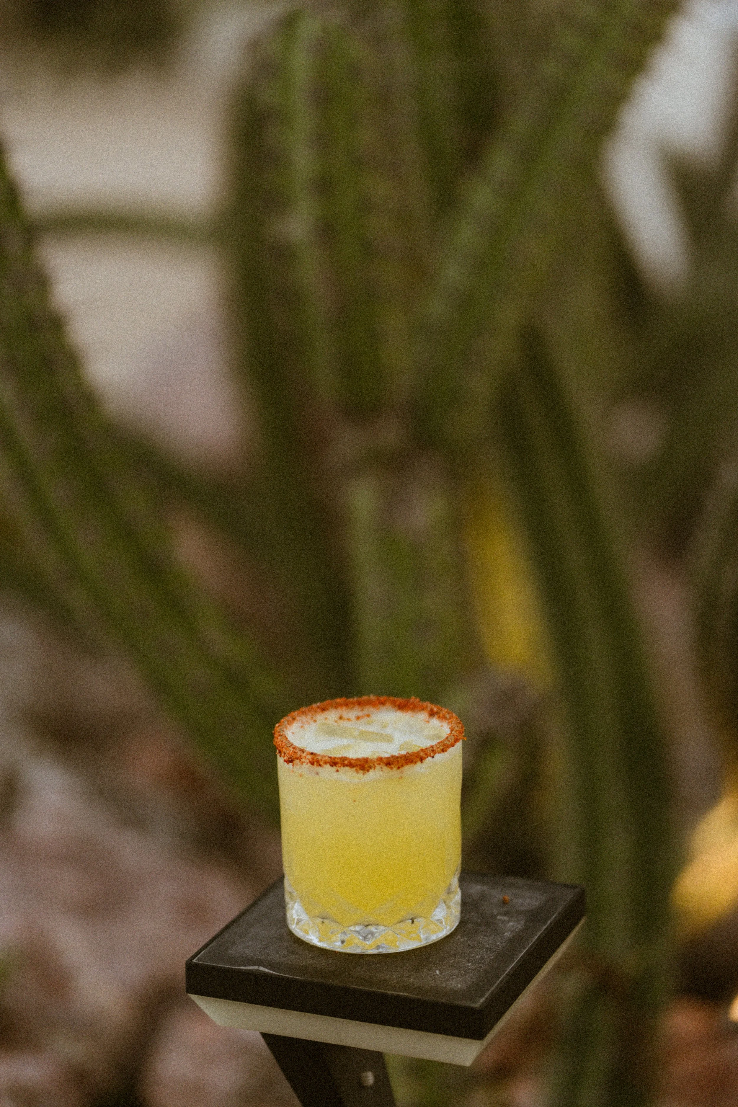 A yellow cocktail in a glass with a salted rim, placed on a small black table.