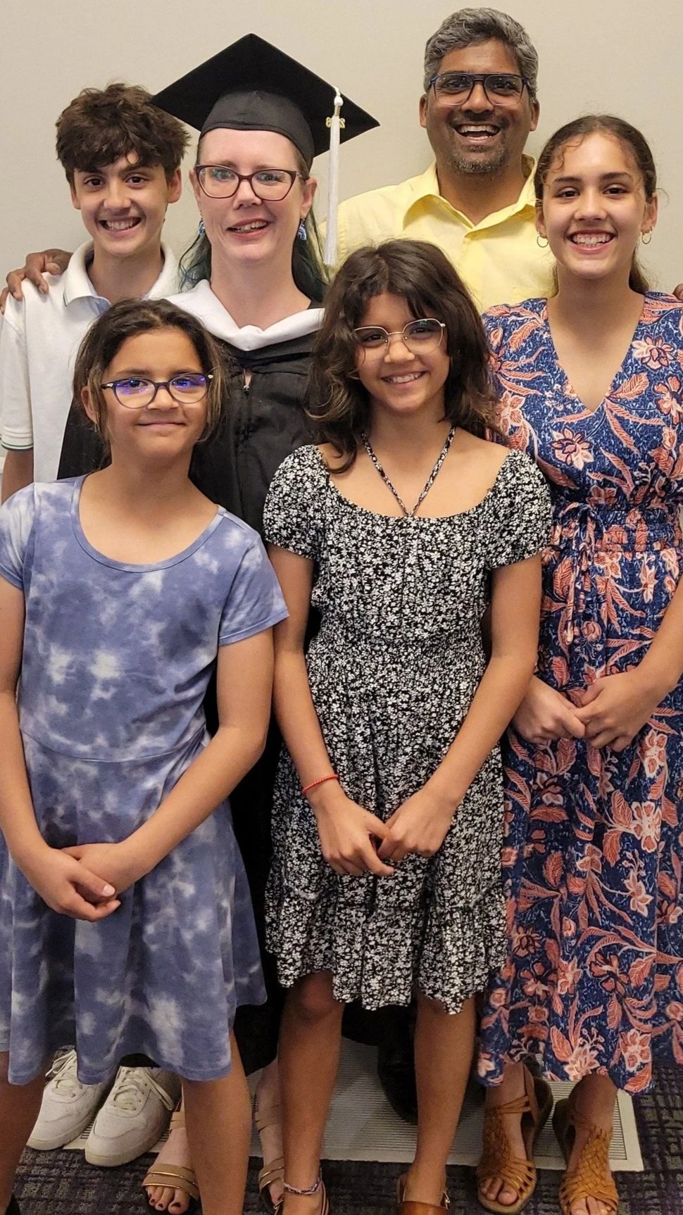 Un groupe de six personnes lors d'une fête de remise des diplômes, composé d'une femme en toge et coiffe, de trois jeunes filles, d'un homme et d'un jeune garçon, tous souriants.