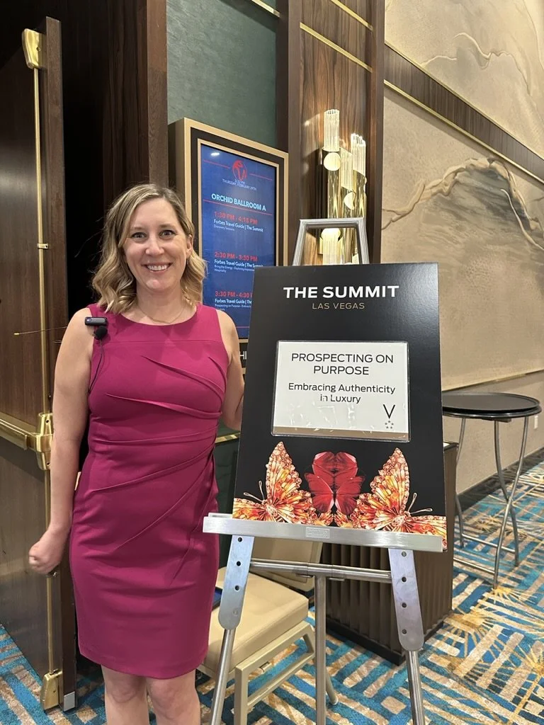 Woman in a pink sleeveless dress standing next to a black sign at The Summit in Las Vegas, with a butterfly graphic and the message 'Prospecting on Purpose: Embracing Authenticity in Luxury'.