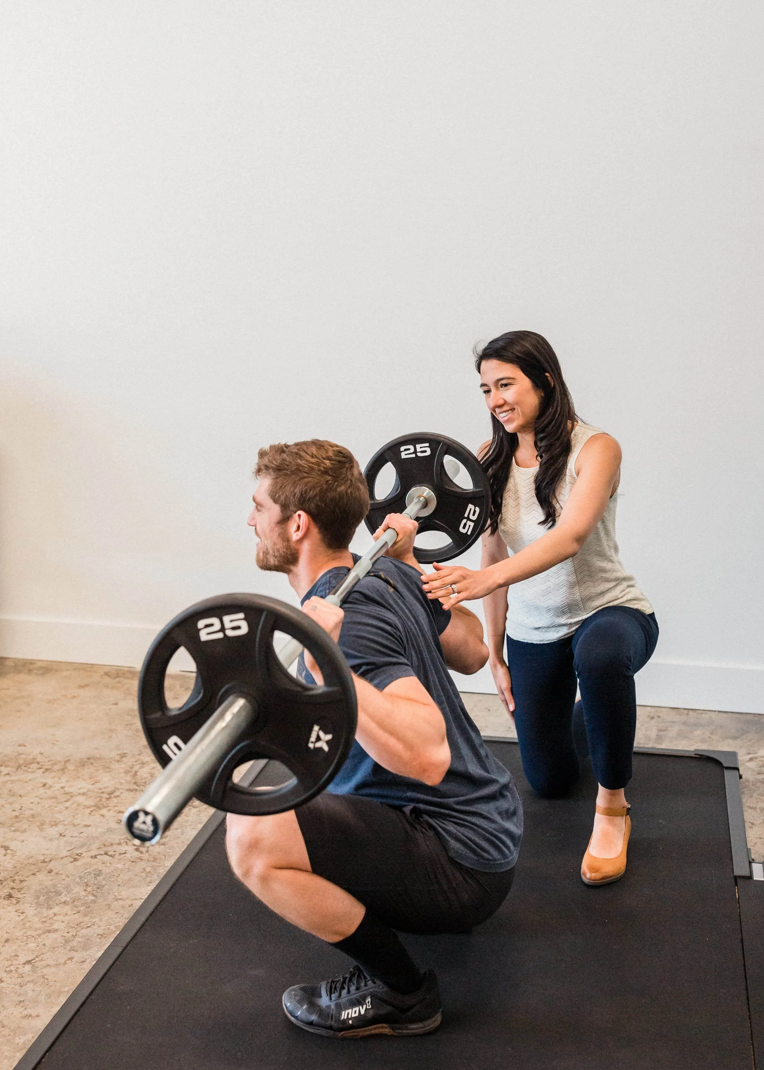 Man squatting with bar bell. Women in Motion PT helping to stabalize back.