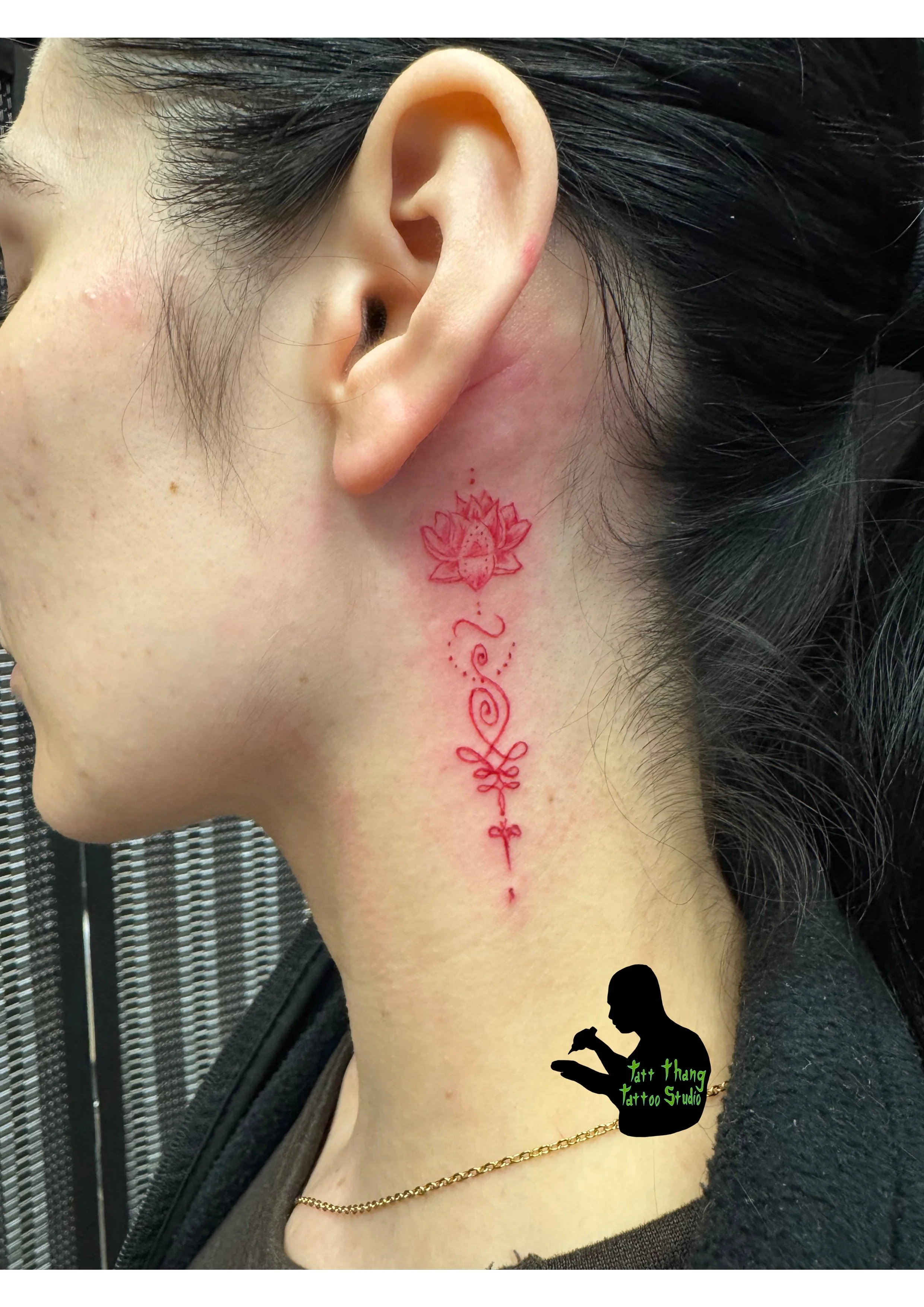 Red outline tattoo of a lotus flower, decorative swirl, and cross on the side of a woman's neck.