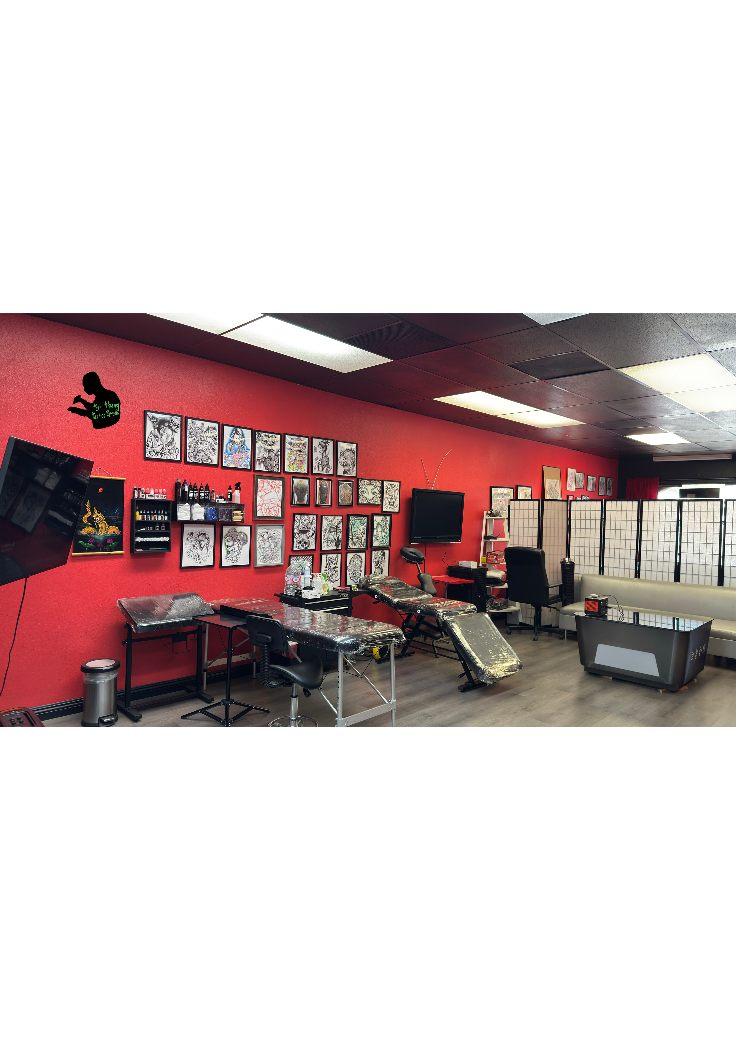 Tattoo studio interior with red walls, artwork, tattoo equipment, a tattoo chair, and a screen divider.