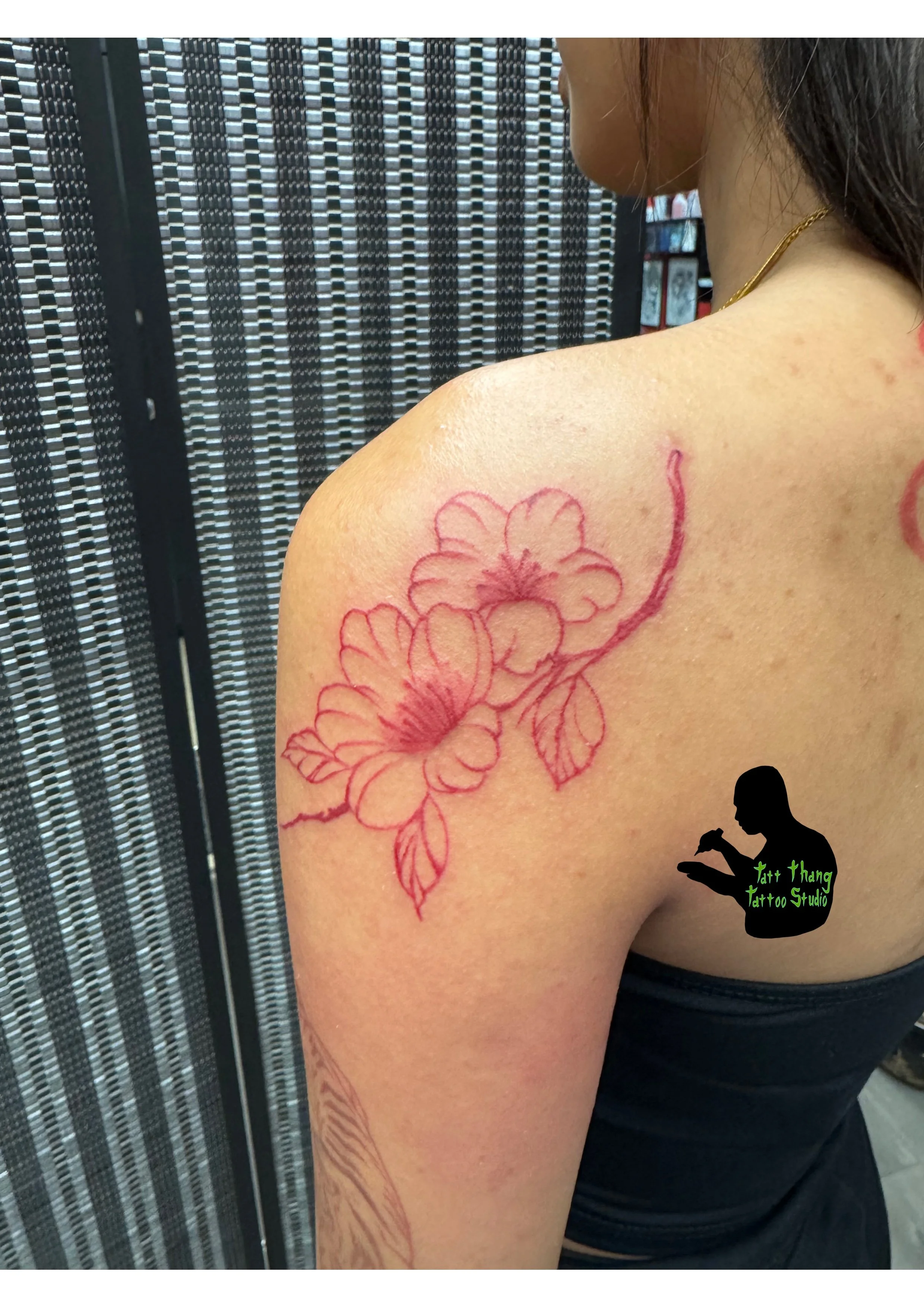 A woman with a floral tattoo red outline on her shoulder and upper arm.
