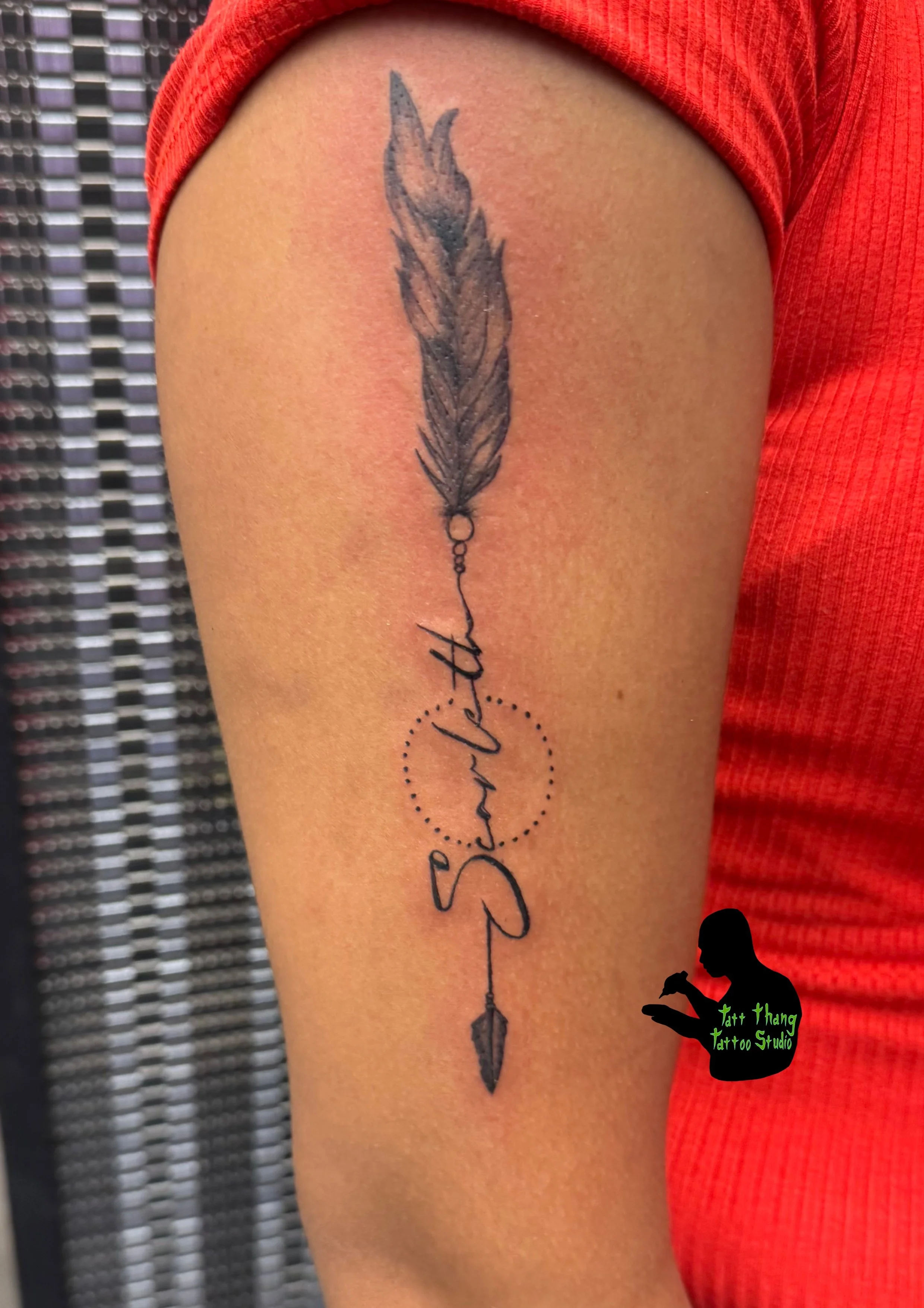Tattoo of a feather, with cursive script, with dotted circles surrounding part of the script.