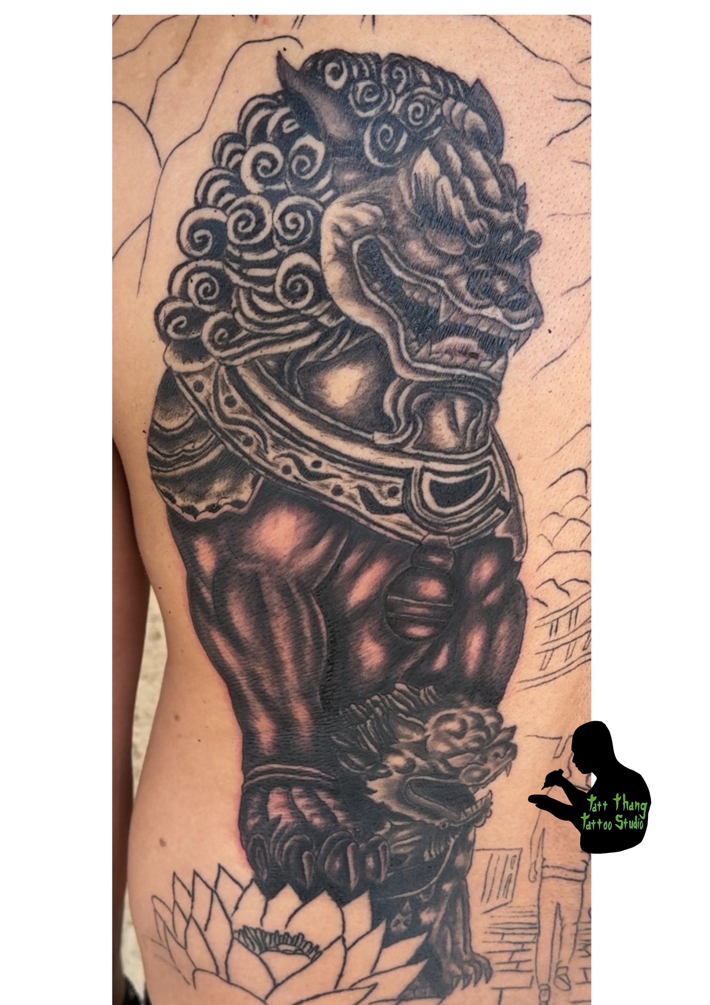 Tattoo of a Fu Dogs, muscular body, and ornate mane with a collar and bell, with a lotus flower at the bottom.
