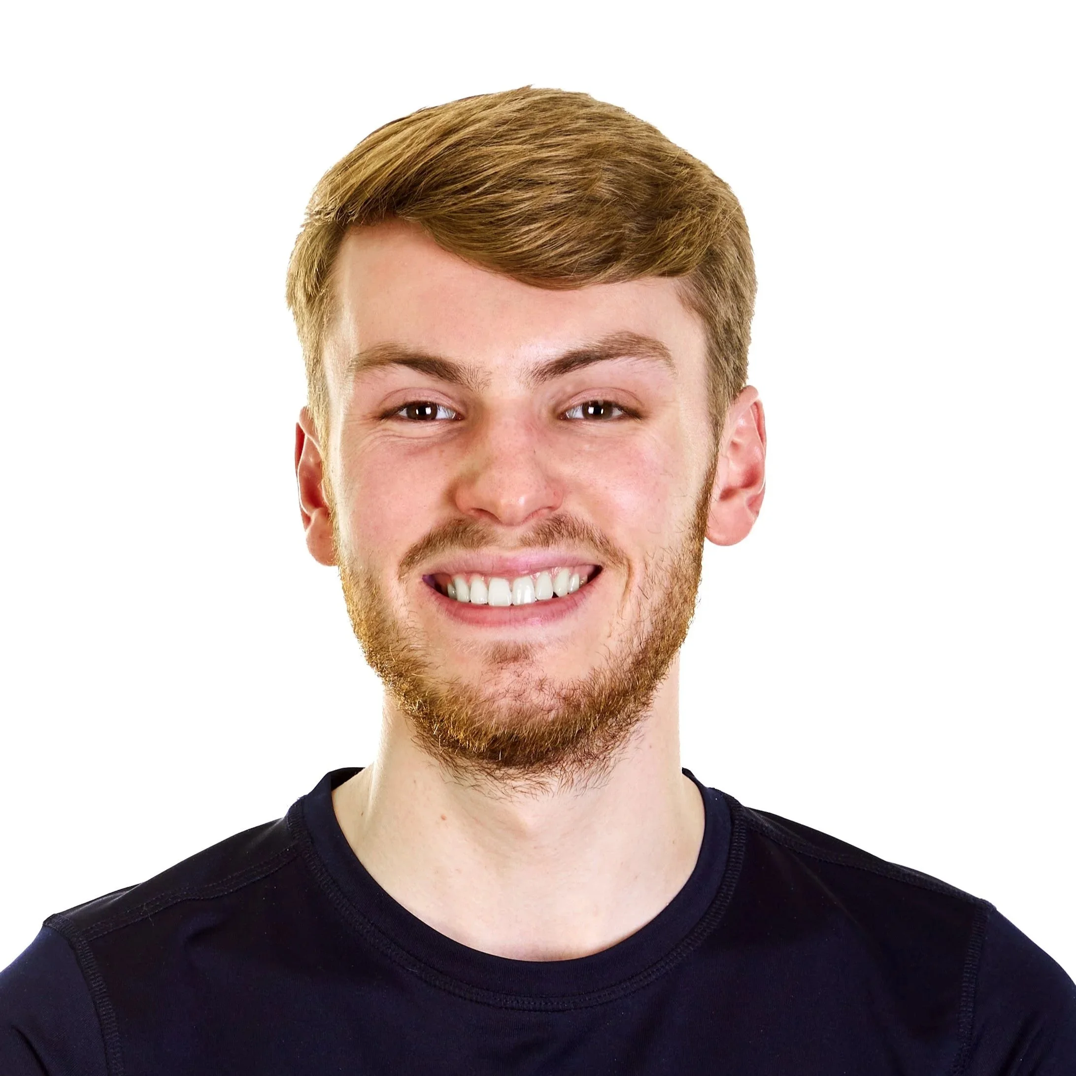 Close-up portrait of a young man with ginger hair, a beard, and a bright smile, wearing a black t-shirt against a plain white background.