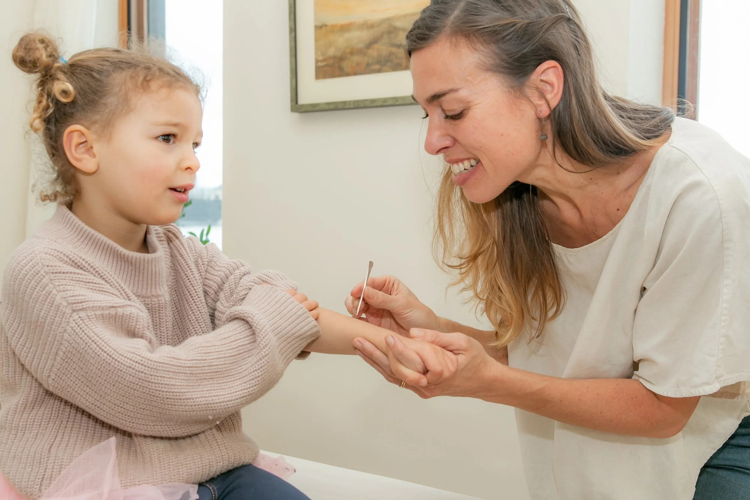 A young girl getting her finger pricked for a blood sample by a woman, possibly a nurse or healthcare provider, in a medical setting.