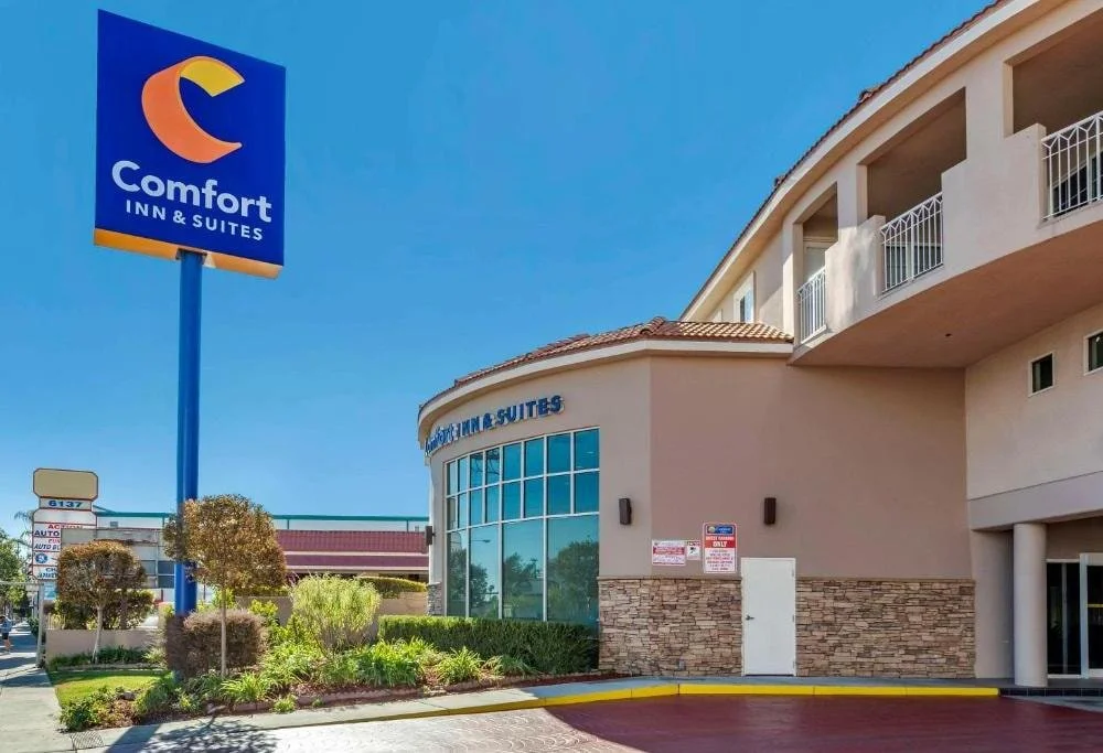 Front view of Comfort Inn & Suites Near Universal – North Hollywood/Burbank with blue sky, hotel facade, and large sign on Lankershim Boulevard.
